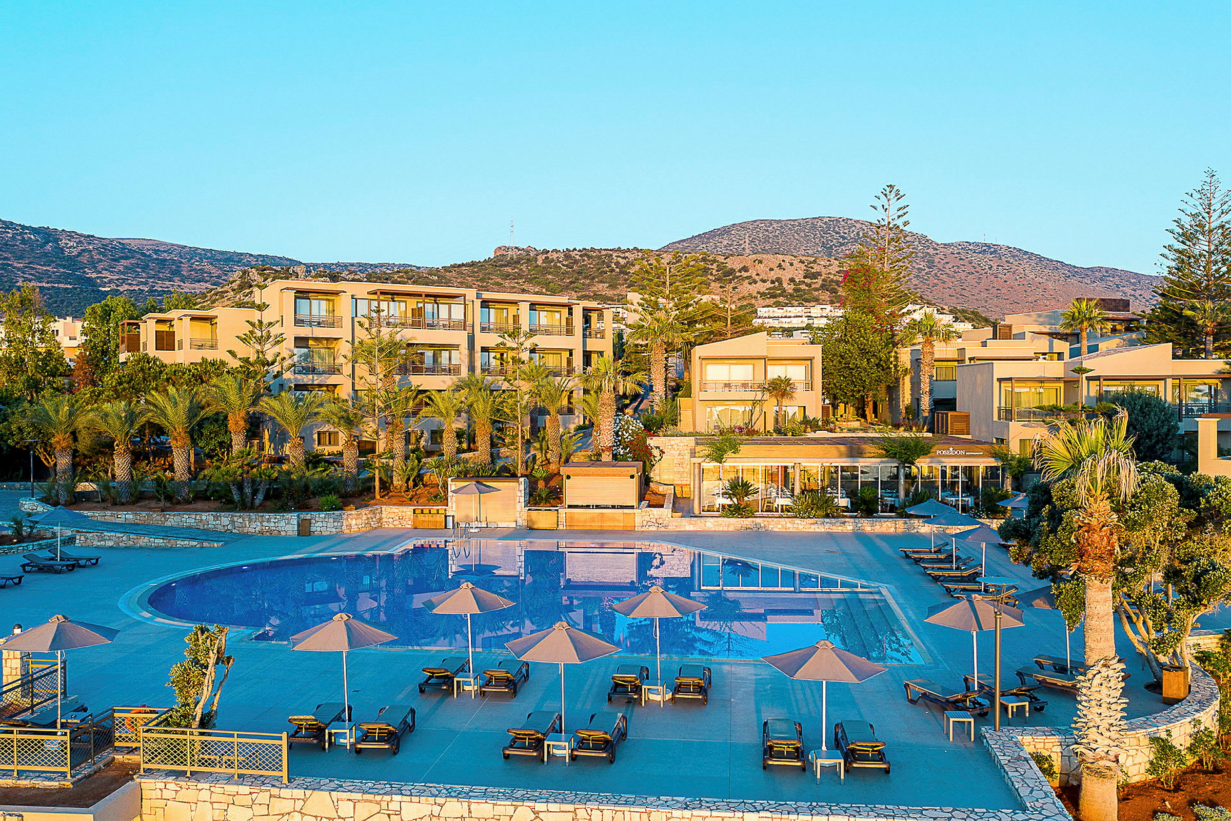 Billede af et resort med pool og omkringliggende bygninger mod en klippe. (AI-genereret tekst)