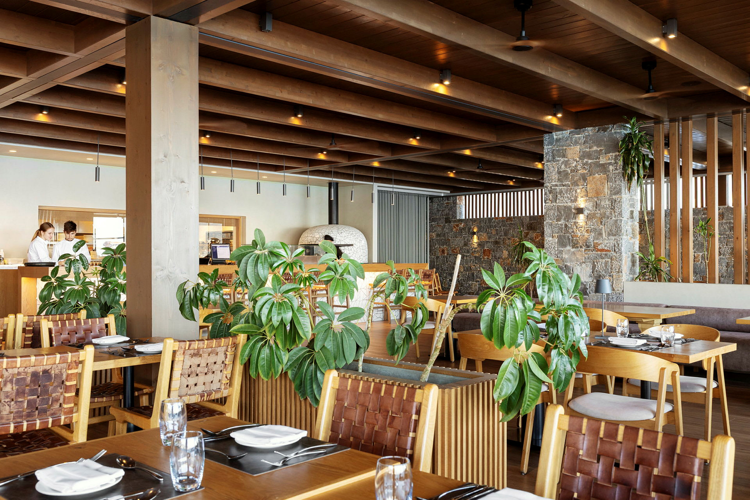 Et moderne restaurantinteriør med træmøbler, grønne planter og stenvægge. (AI-genereret tekst)