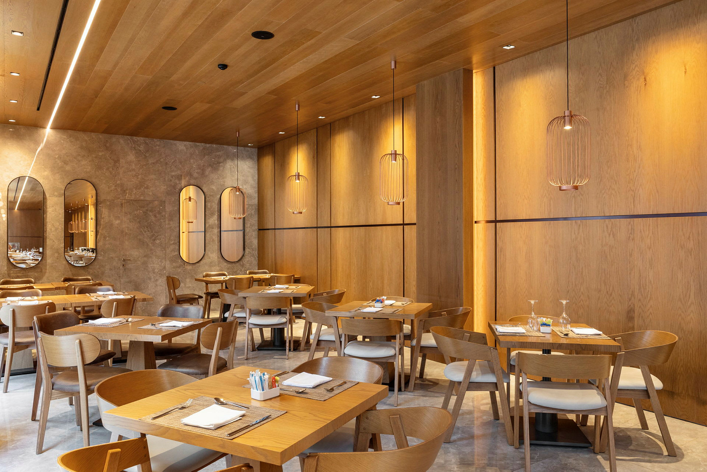 En moderne restaurant med træpaneler på vægge og loft, elegante hængelamper og opdækkede borde med træstole. (AI-genereret tekst)