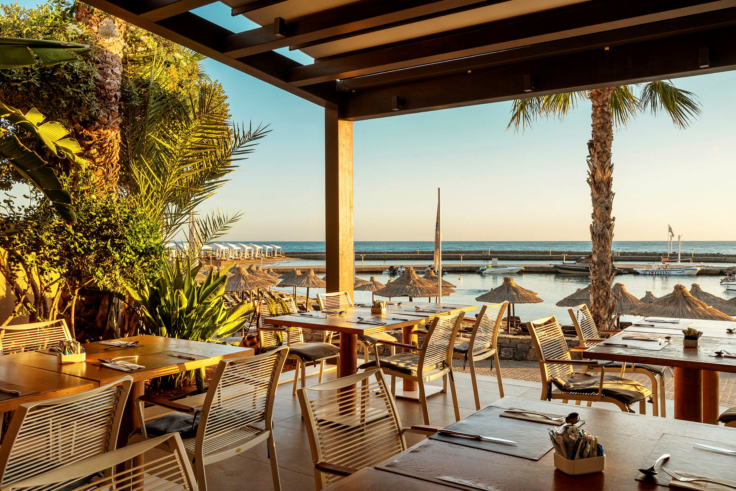 Udsigt fra en restaurant med havet i baggrunden og parasoller på stranden. (AI-genereret tekst)