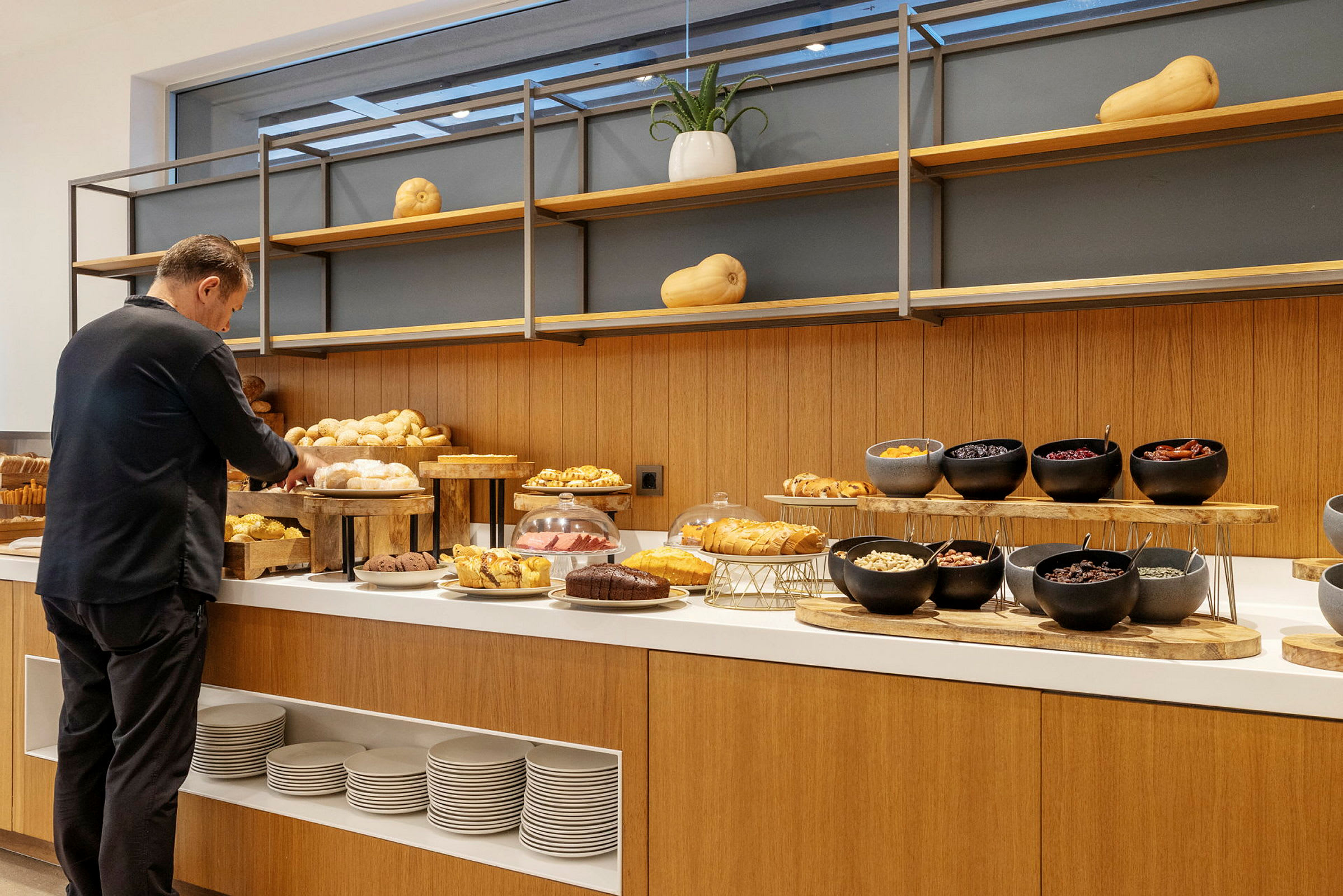 En person ved en buffet fyldt med bagværk såsom brød og muffins samt skåle med forskellige ingredienser. (AI-genereret tekst)