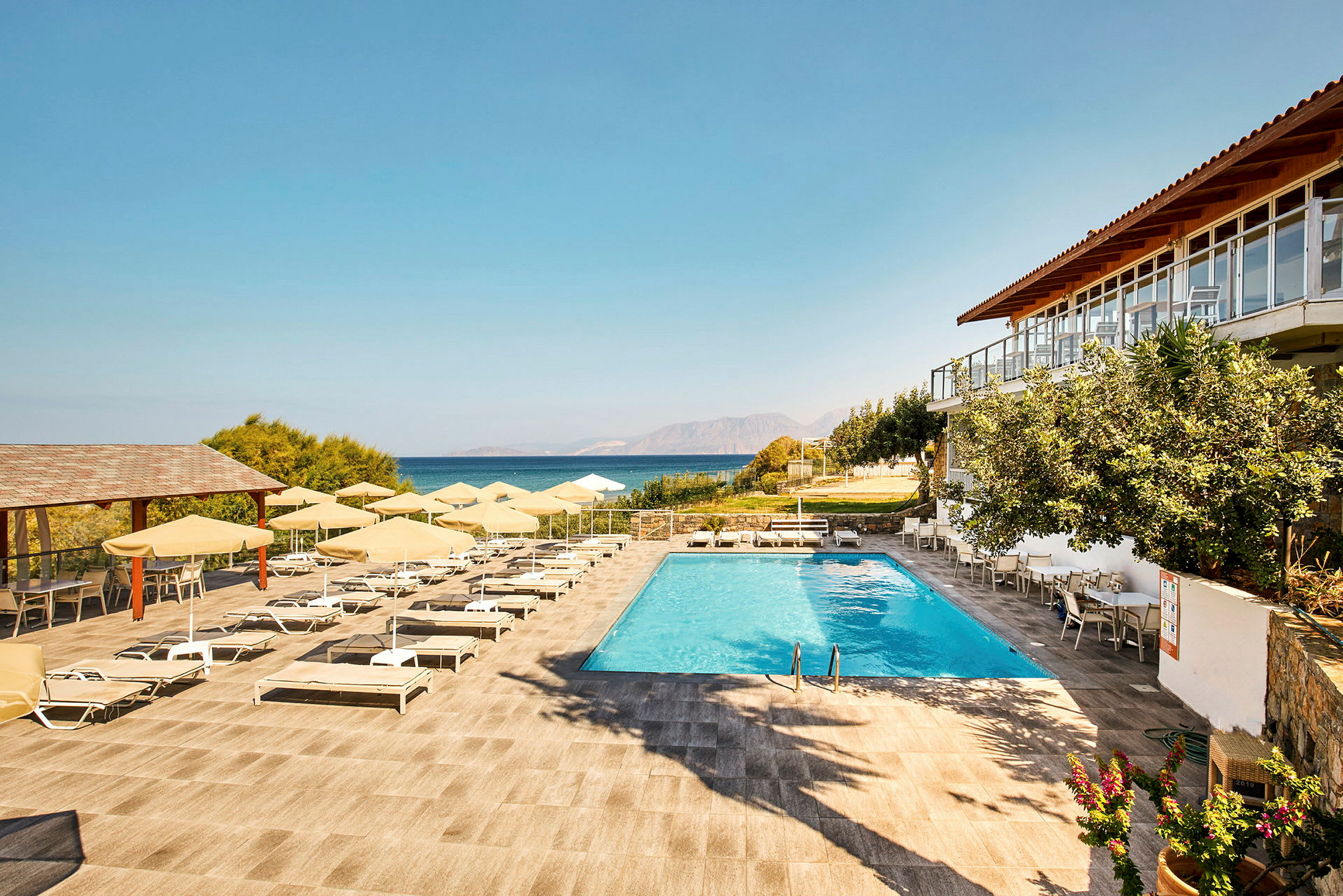 En pool med liggestole og parasoller på en terrasse med udsigt over havet. (AI-genereret tekst)