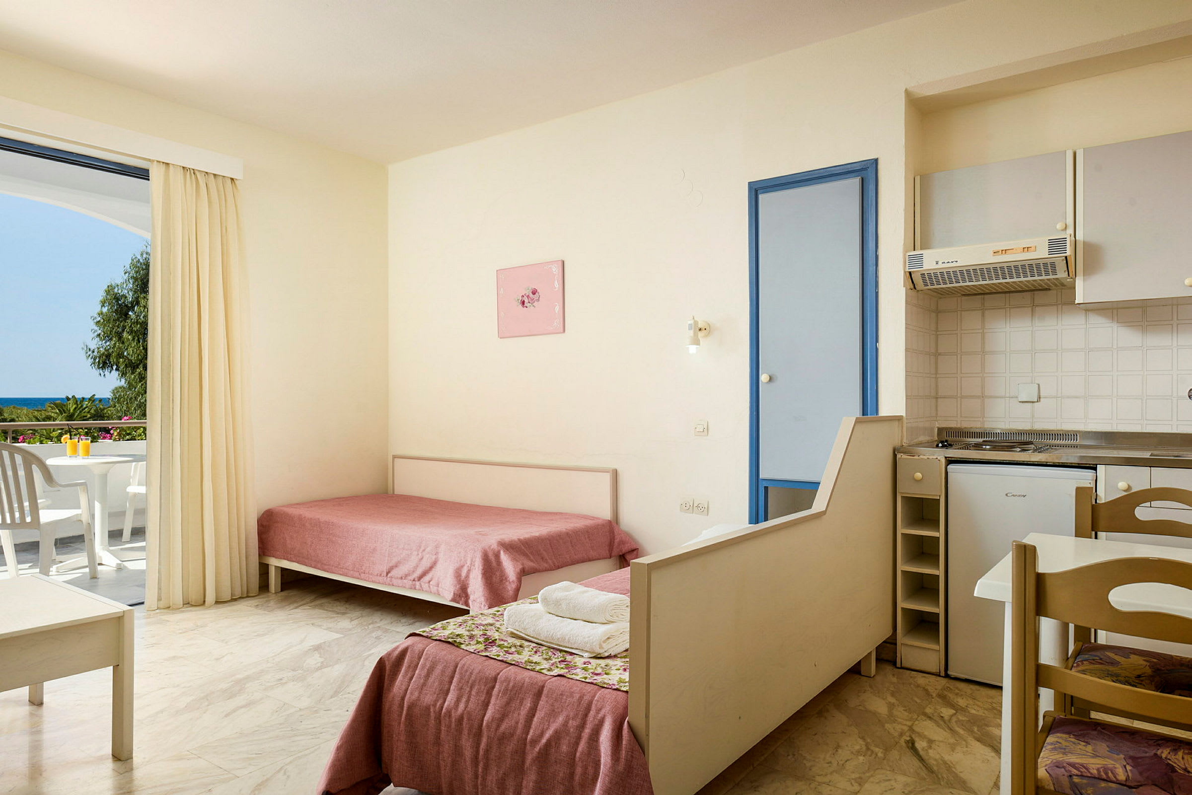 Interiør af et hotelværelse med to enkeltsenge, et lille køkken og en balkon med udsigt. (AI-genereret tekst)