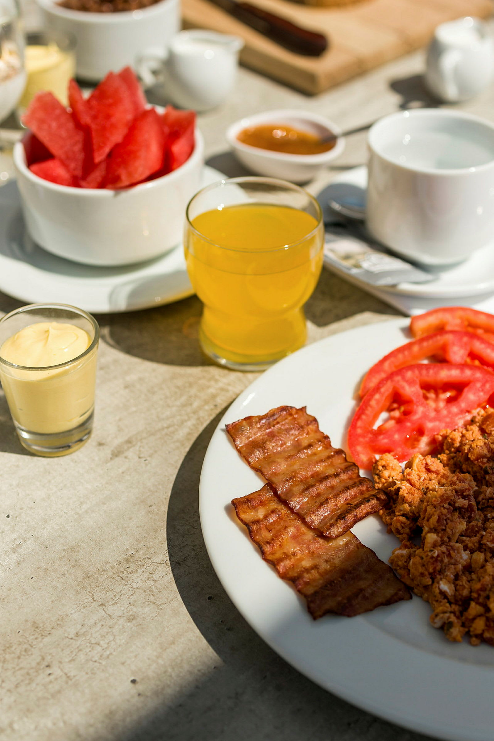 En morgenmad med bacon, skivede tomater, røræg og forskellige drikke. (AI-genereret tekst)