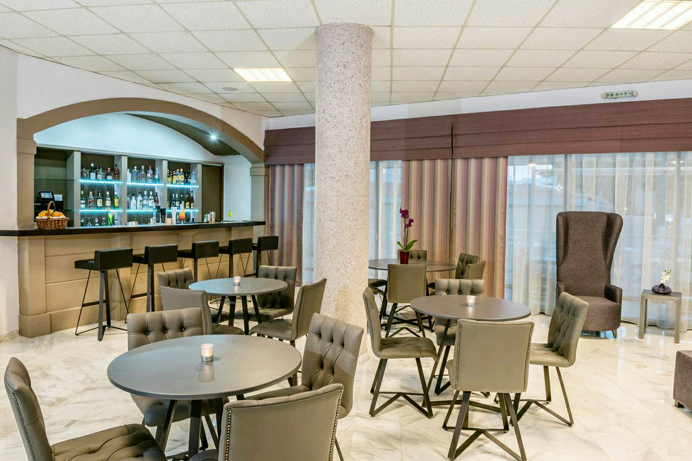 Billede af en hotelbar med flere borde og stole samt en bardisk med barstole. (AI-genereret tekst)