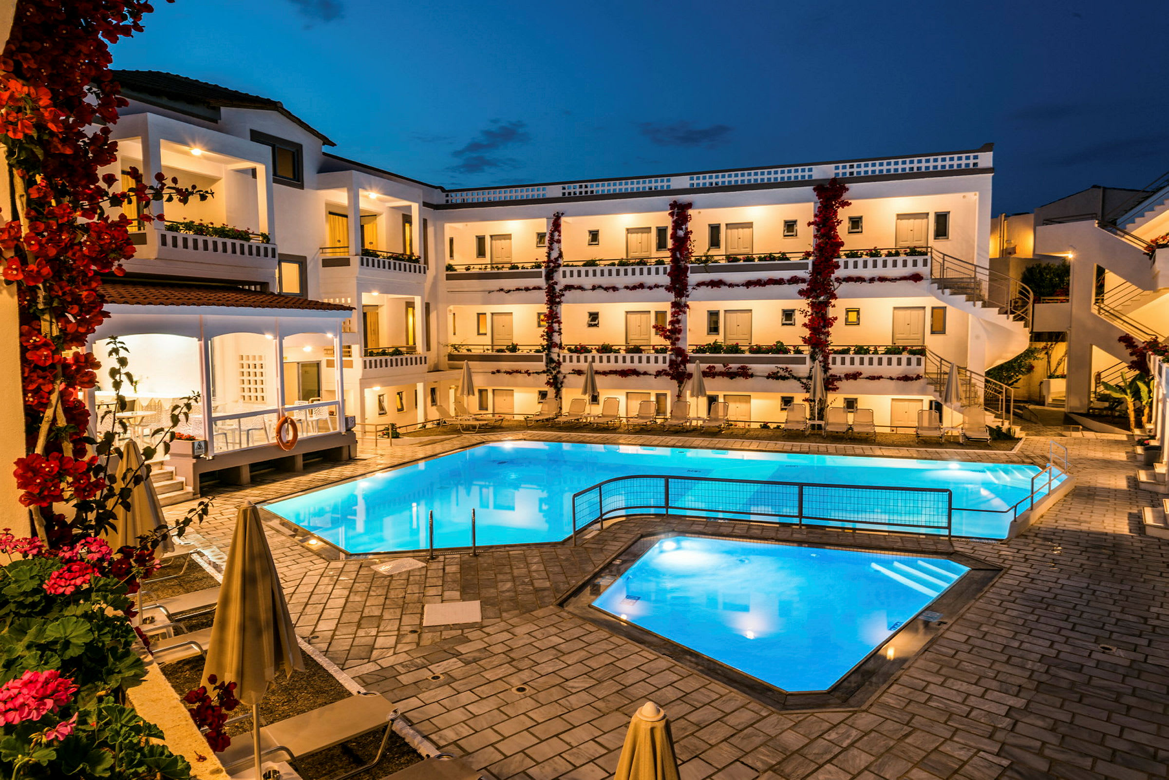 Billede af en oplyst hotelpool og bygning om aftenen. (AI-genereret tekst)
