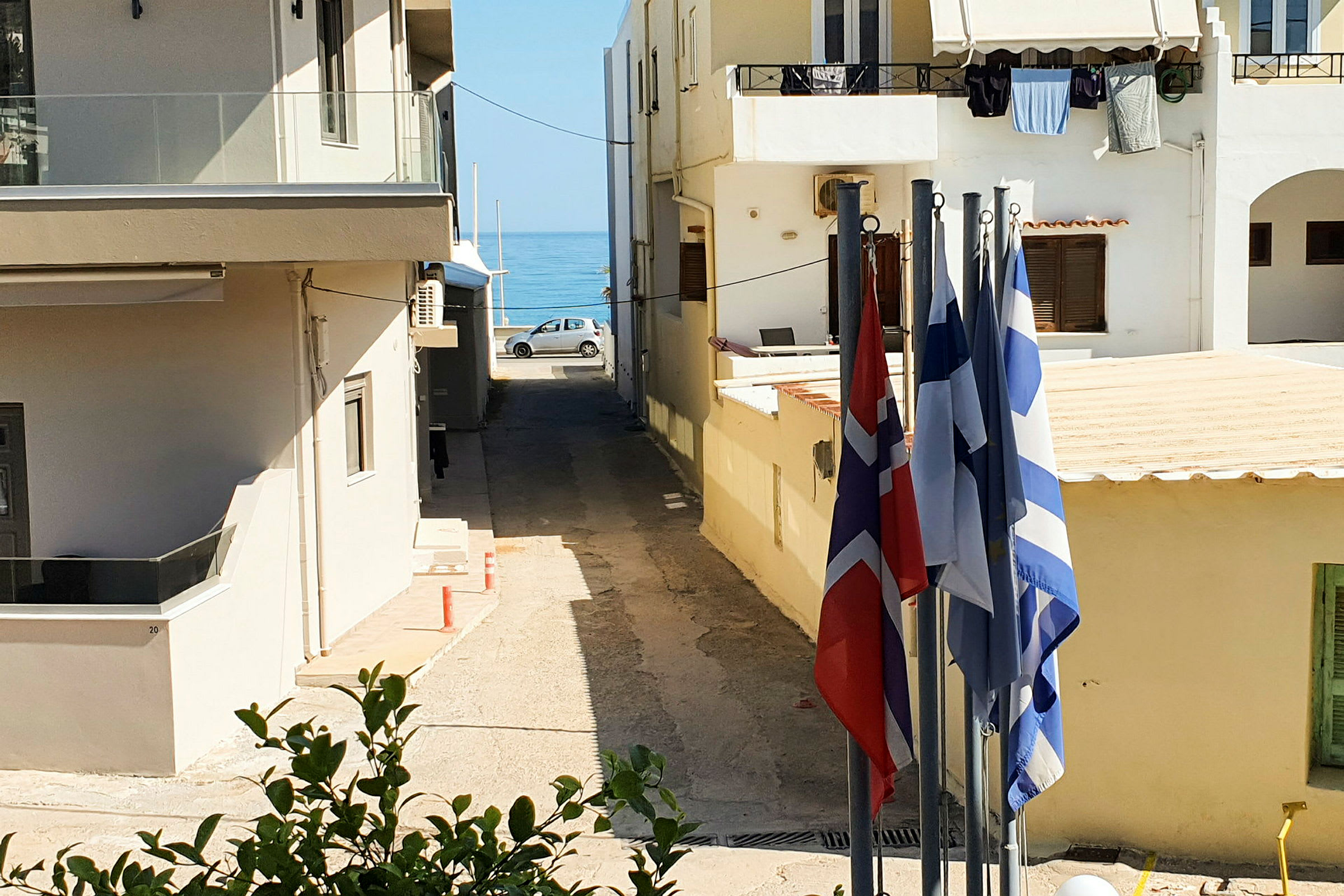 Udsigt over en lille gade med bygninger på begge sider og havet synligt i baggrunden. Flere flag er placeret i forgrunden. (AI-genereret tekst)