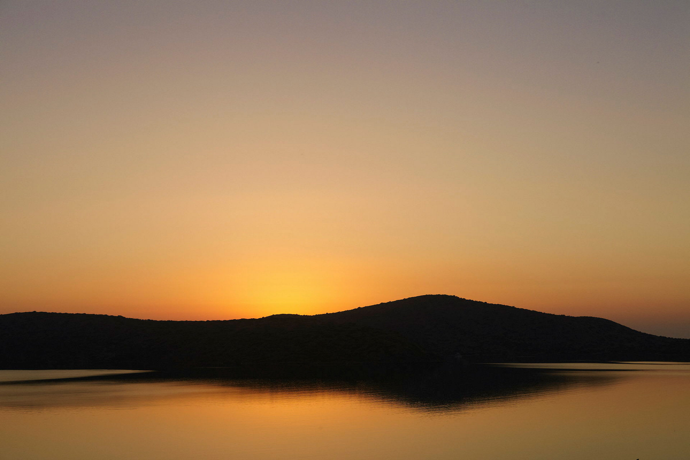 Solnedgang over en sø med silhuetter af bakker. (AI-genereret tekst)