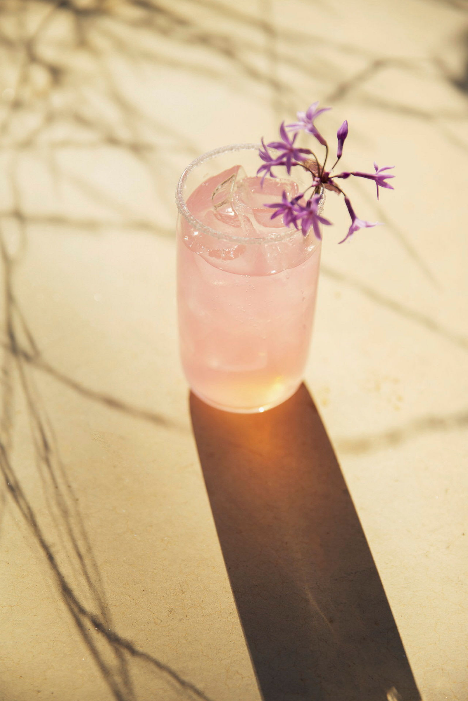 Et glas med en lyserød drik og is, dekoreret med lilla blomster. (AI-genereret tekst)