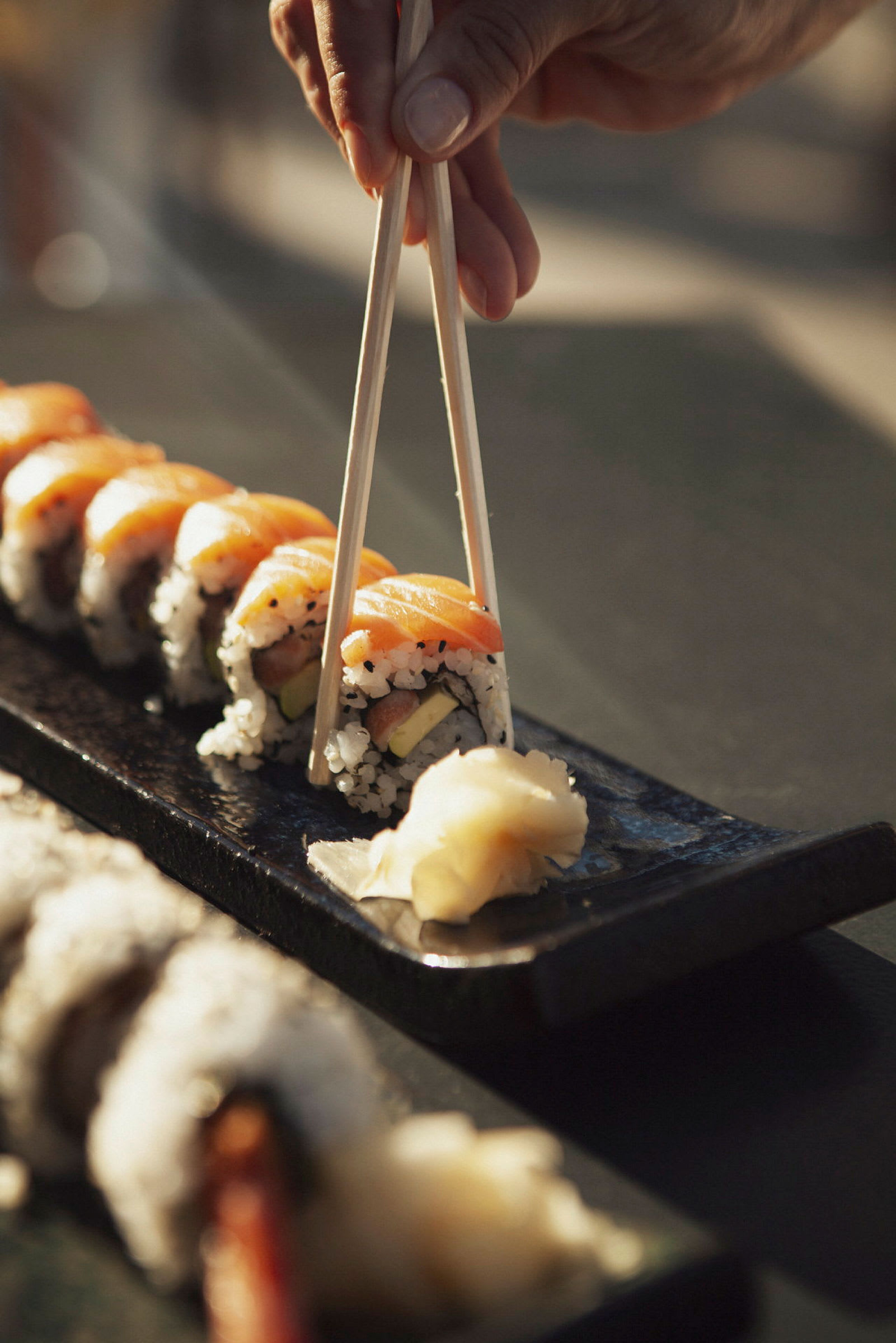 Hånd holder spisepinde og tager sushi fra et fad. (AI-genereret tekst)