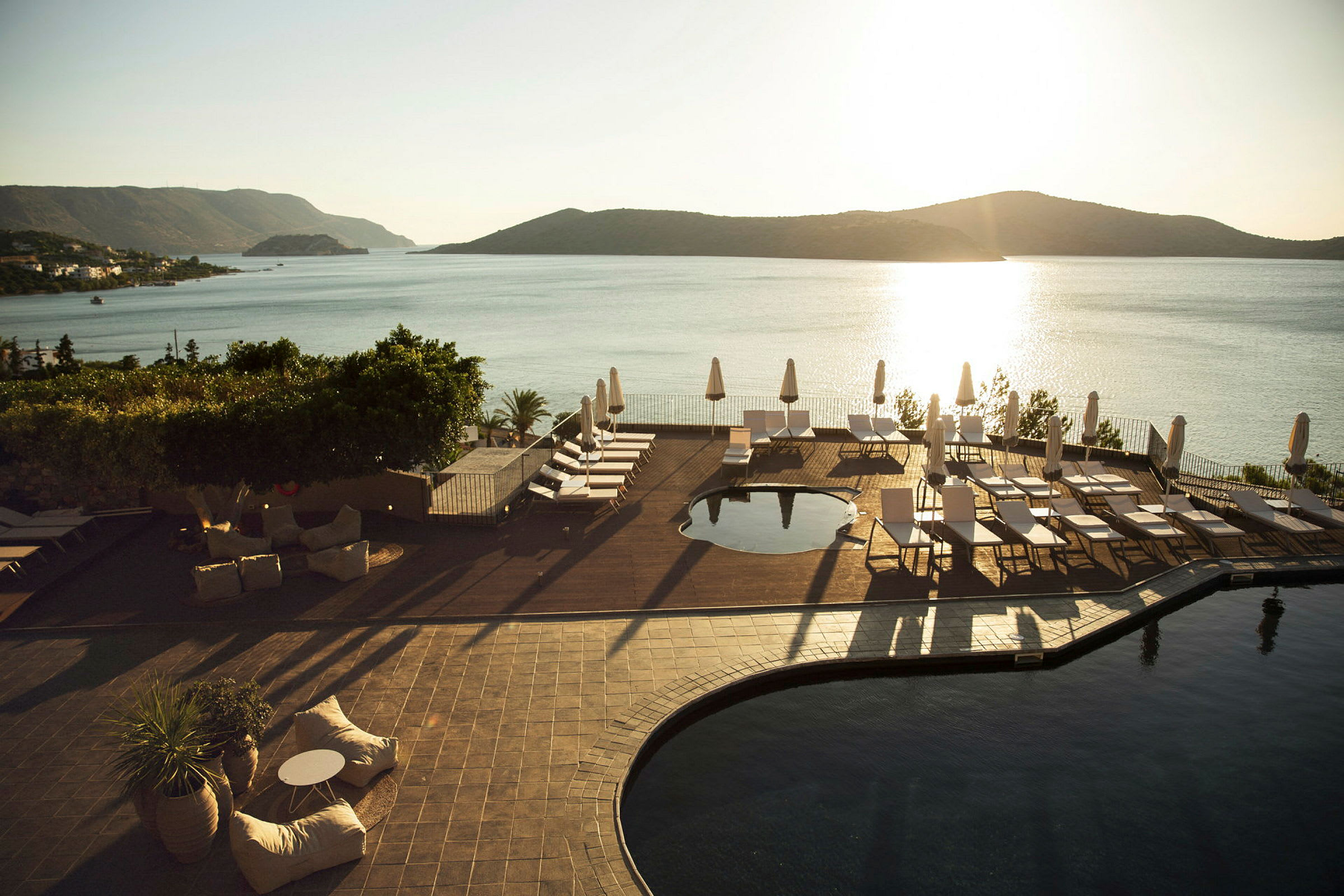 Et hotelpoolområde med liggestole og parasoller nær havet med en solnedgang. (AI-genereret tekst)