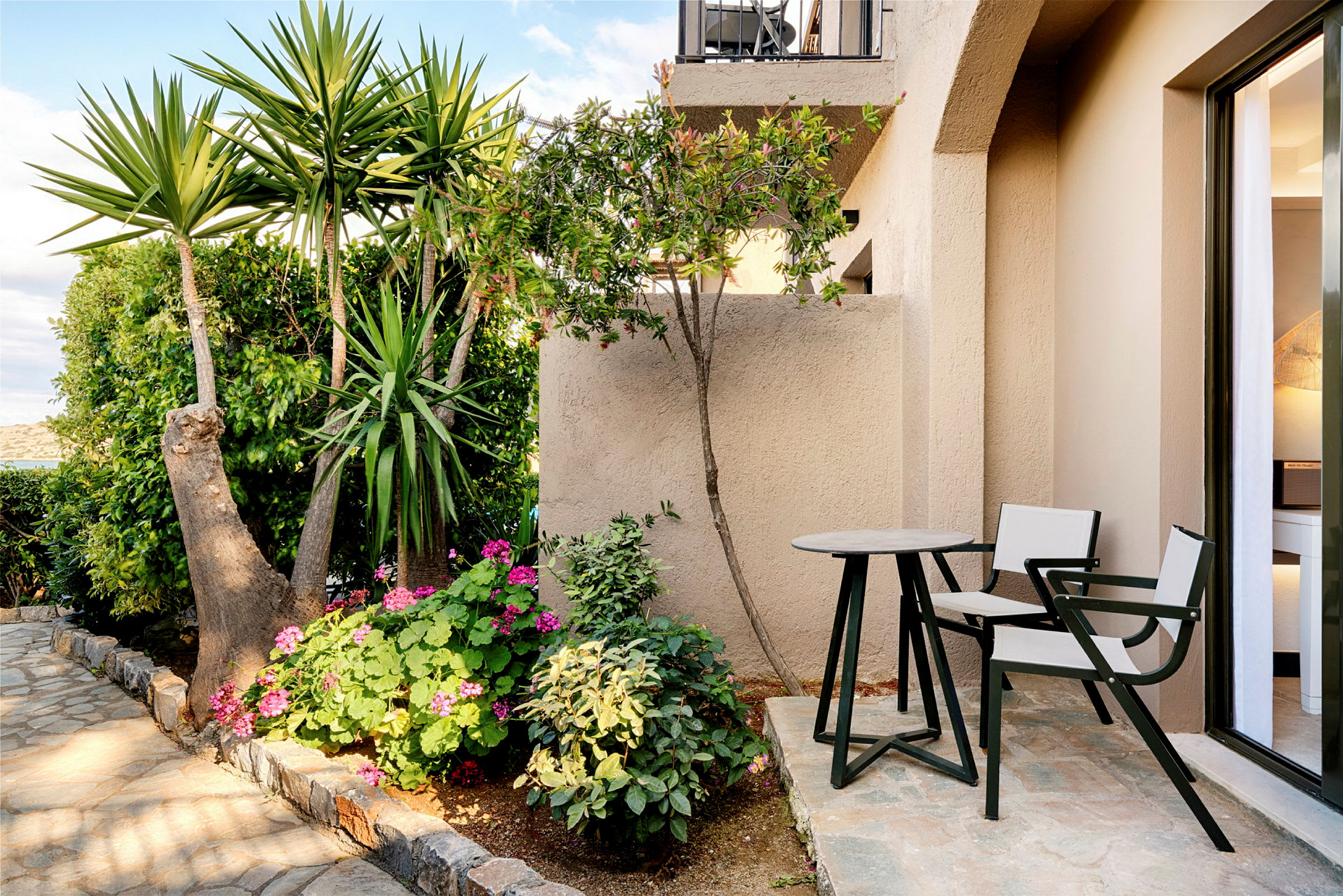 En lille terrasse med bord og to stole, omgivet af planter og blomster. (AI-genereret tekst)