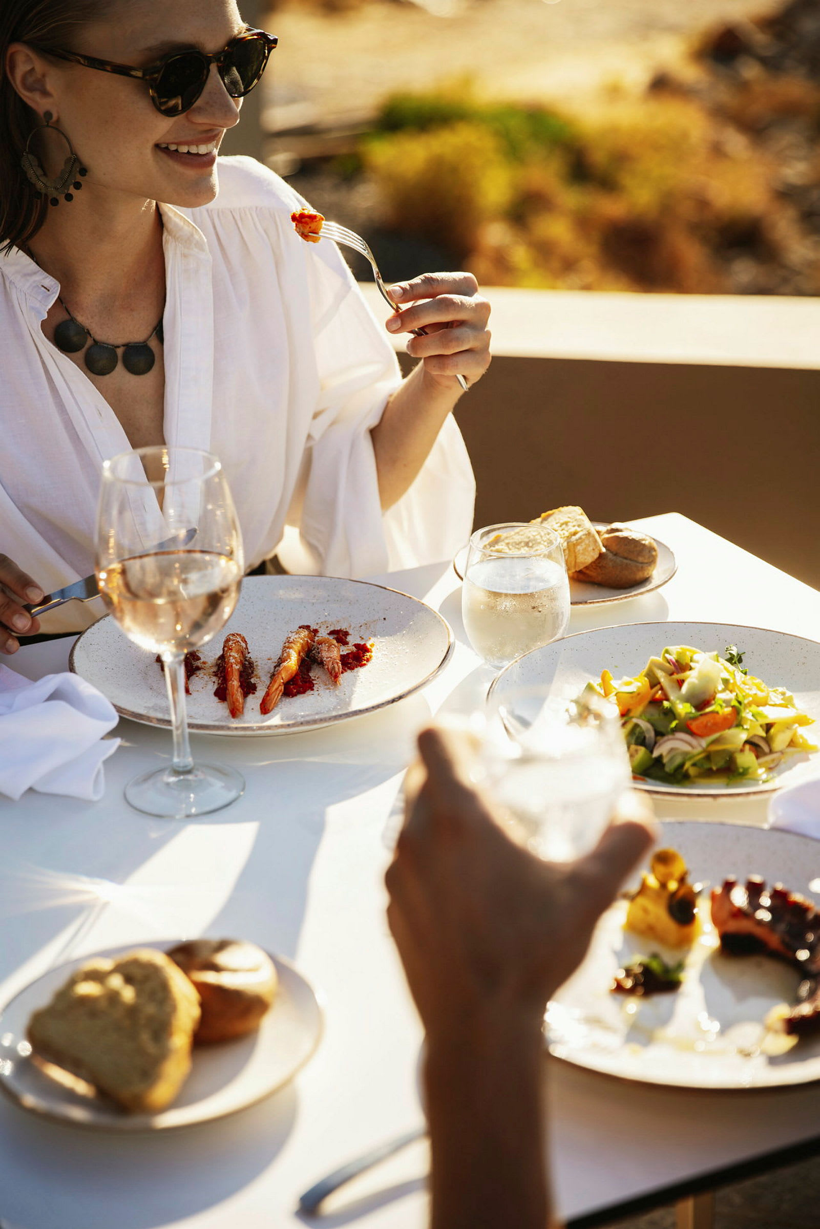 Person, der sidder ved et bord med et måltid og et glas vin udendørs. (AI-genereret tekst)