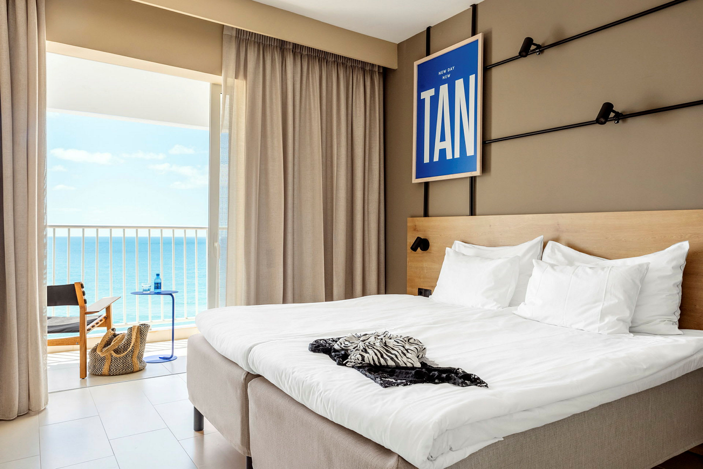 Hotelværelse med en dobbeltseng og udsigt til havet gennem altandøren. (AI-genereret tekst)