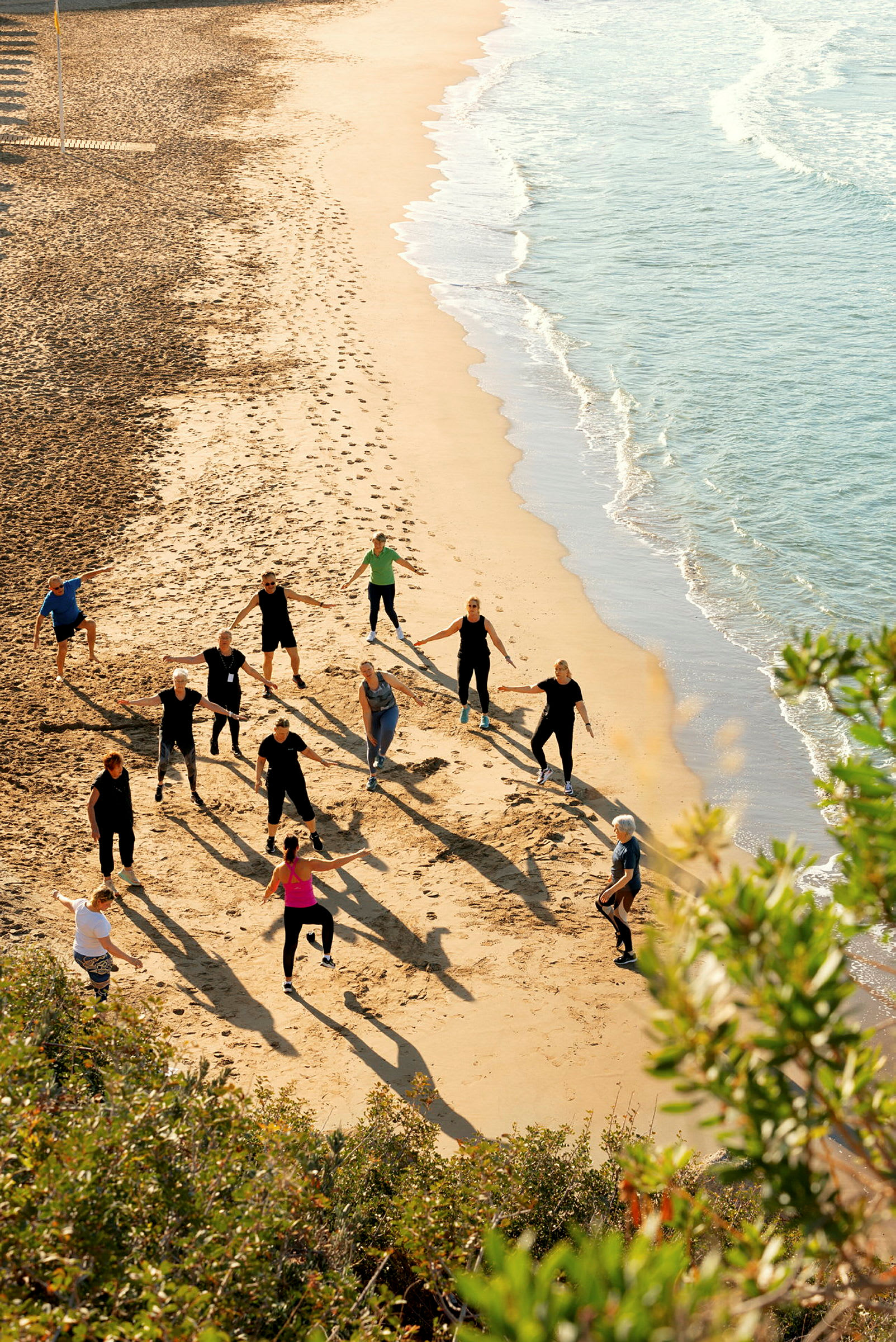 En gruppe mennesker udfører træningsaktiviteter på en sandstrand tæt på havet. (AI-genereret tekst)