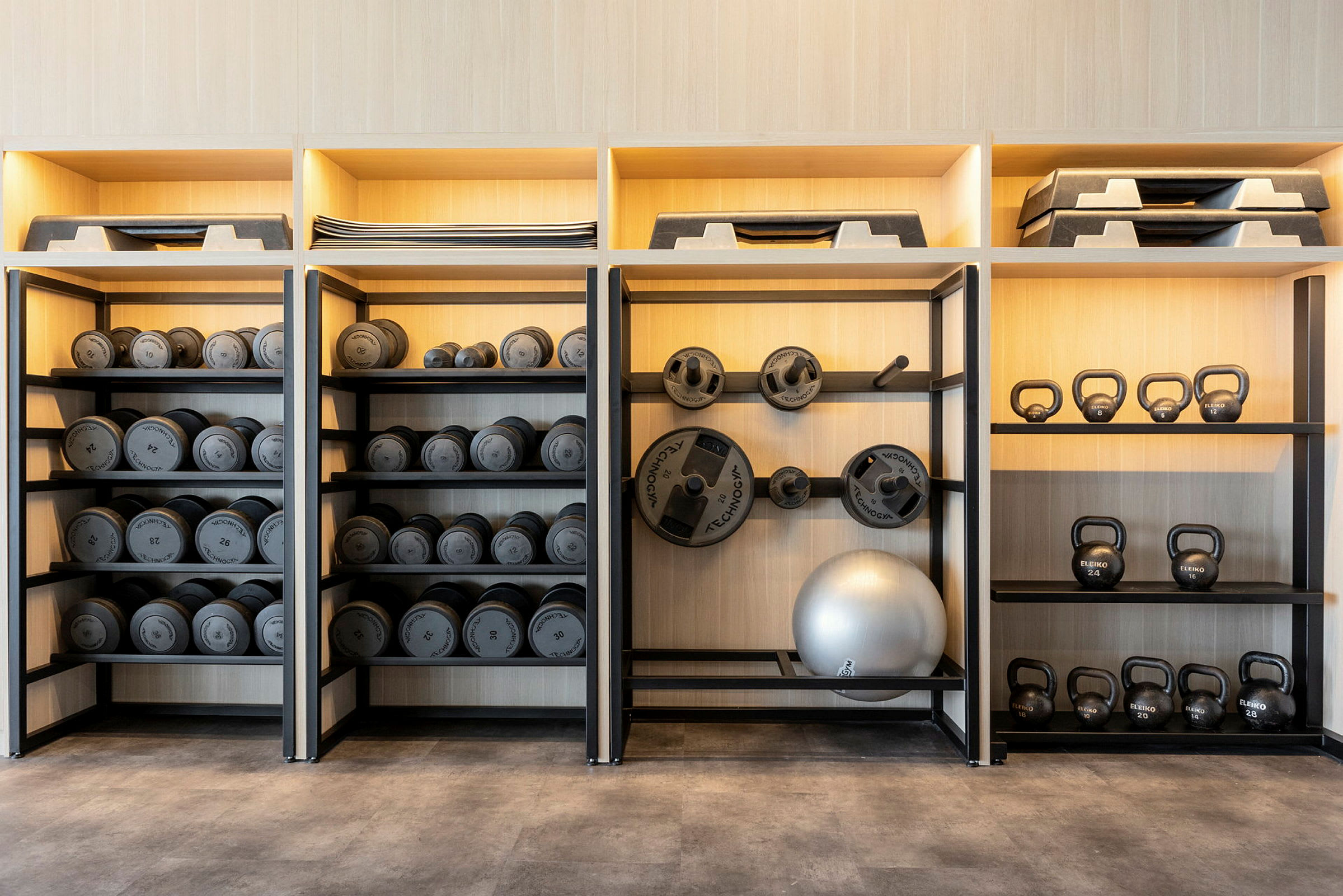Hylde med håndvægte, vægtskiver, kettlebells og træningsudstyr. (AI-genereret tekst)