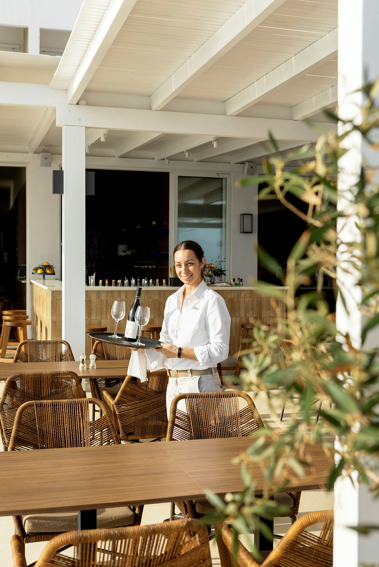 Serveringspersonale bærer en bakke med vin og glas på en restaurantterrasse. (AI-genereret tekst)
