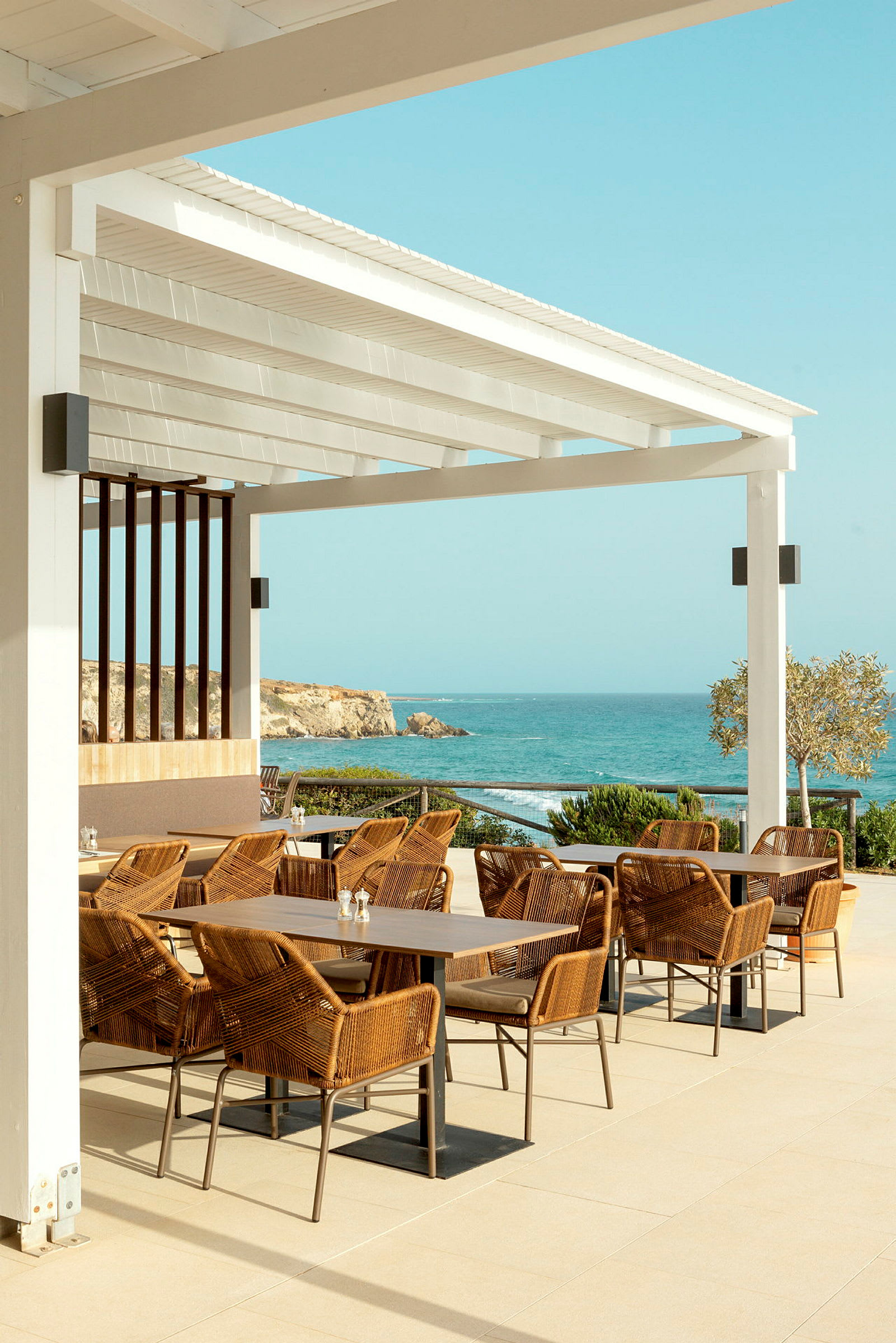 Terrasse med borde og stole samt udsigt over havet. (AI-genereret tekst)