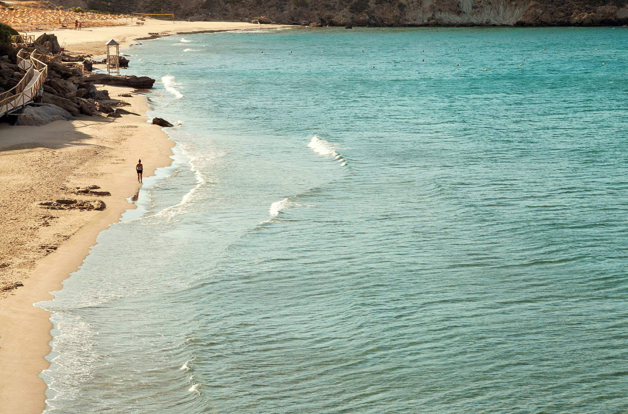 Strand med klart vand og en person, der går langs vandkanten. (AI-genereret tekst)