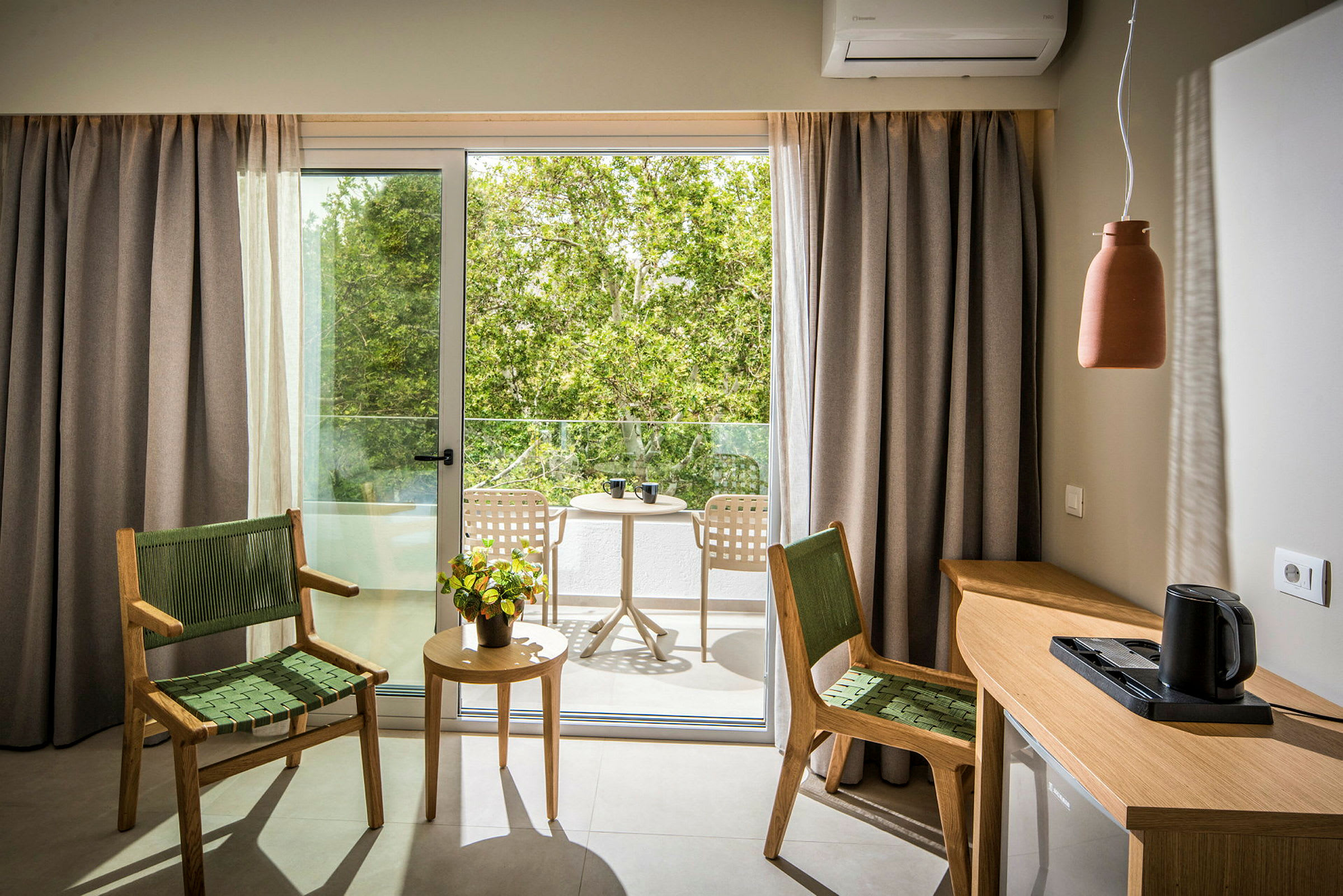 Et rum med to stole og et bord foran en glasdør, der fører ud til en balkon med yderligere møbler omgivet af grønt. (AI-genereret tekst)