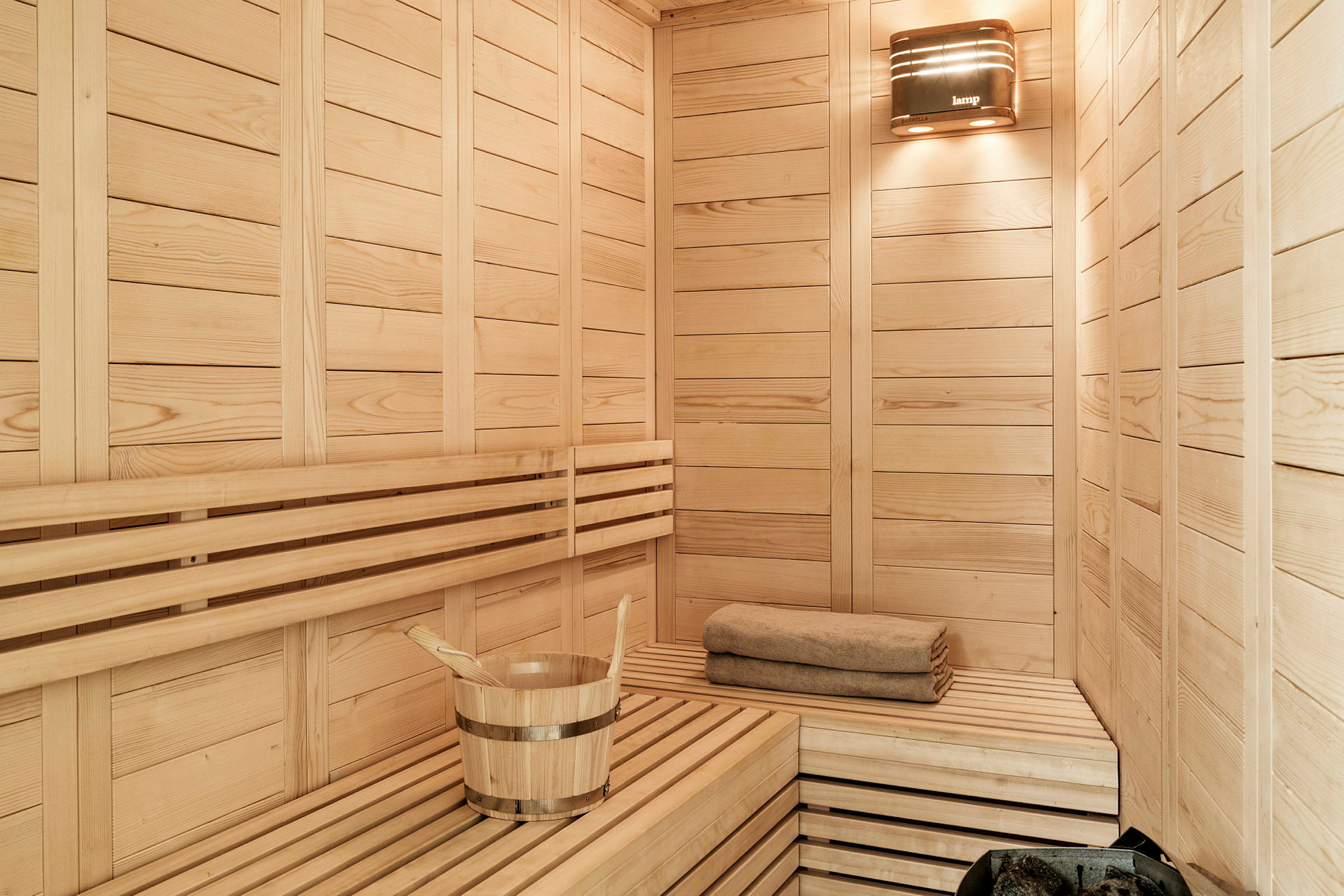 En sauna med træpaneler, en spand med en skovl og et foldet håndklæde. (AI-genereret tekst)