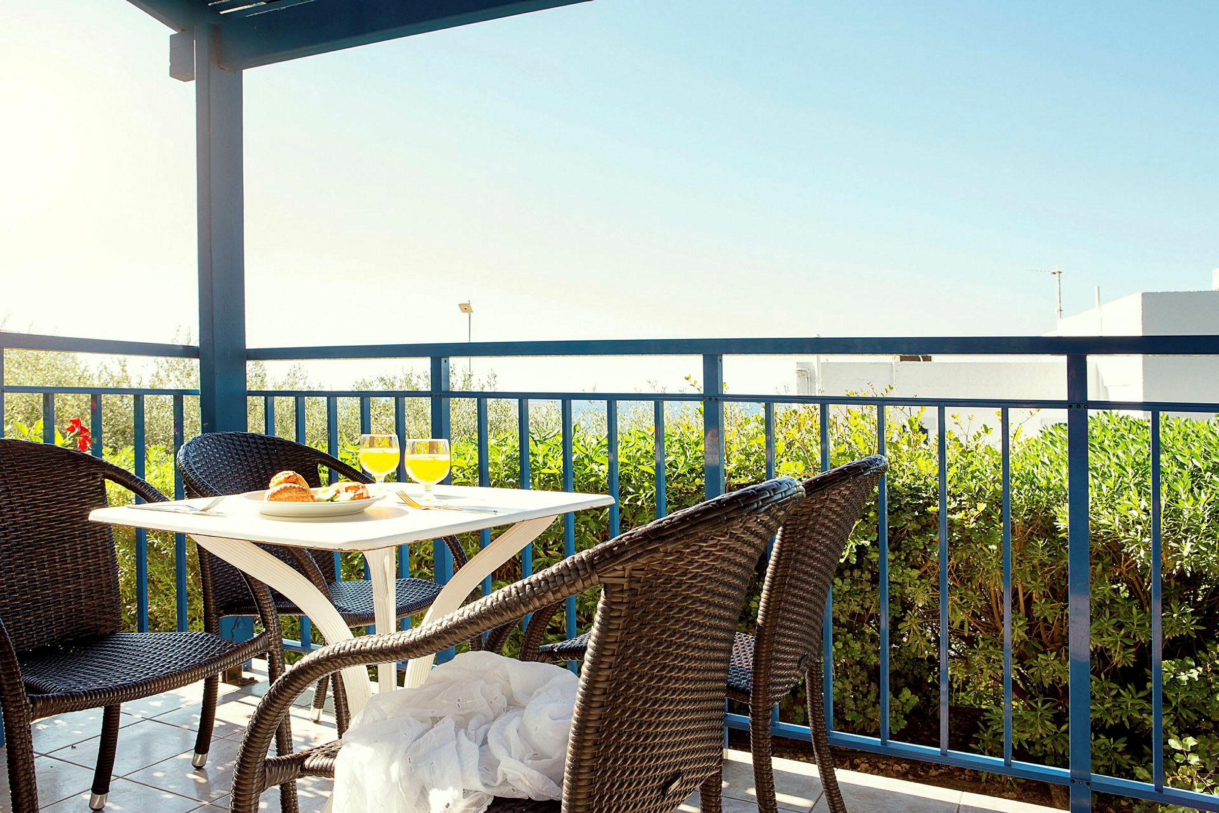 Terrasse med bord og fire rottingstole, udsigt til grønt og blå himmel. (AI-genereret tekst)