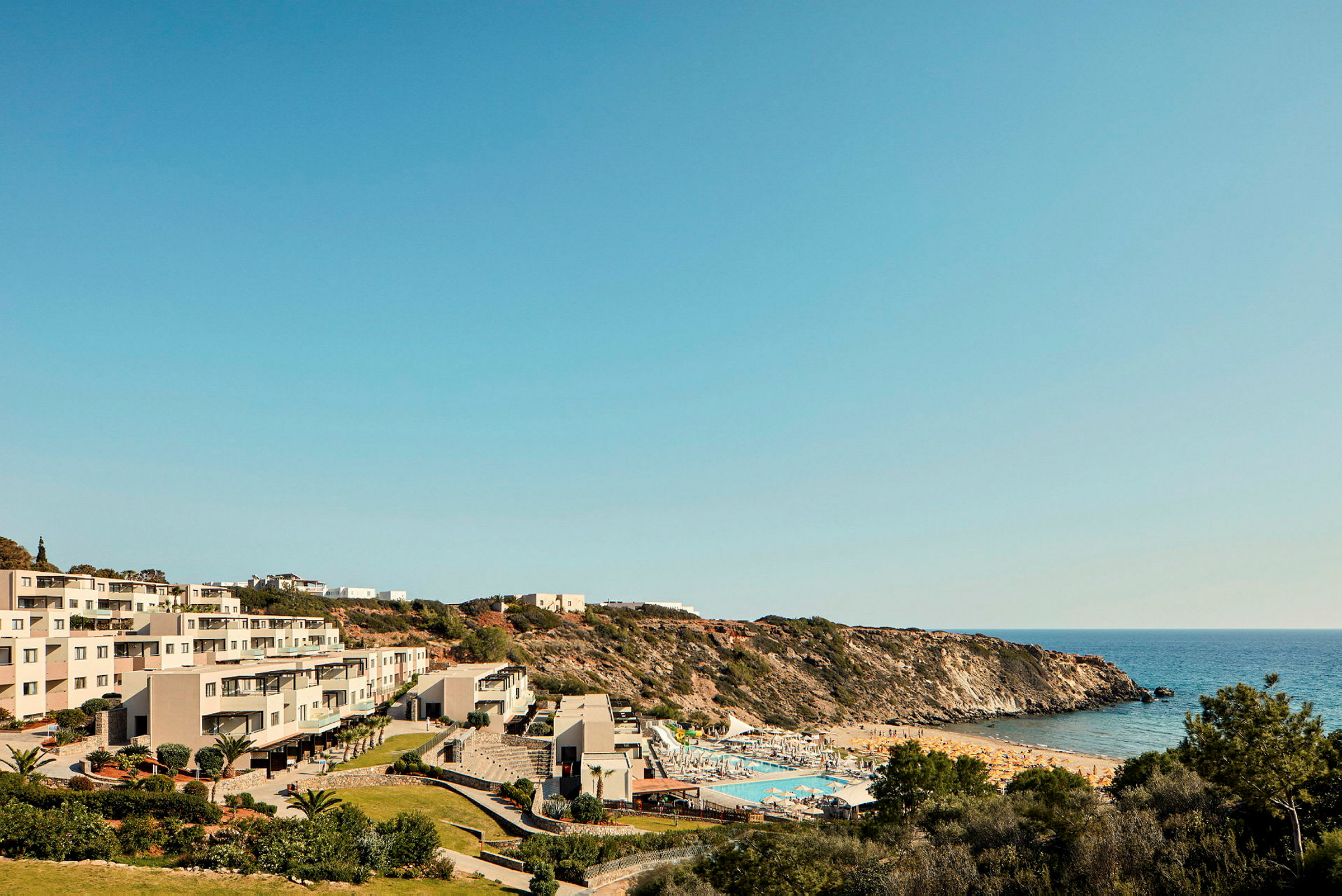 Hotelbygninger i nærheden af en pool og en sandstrand ved havet. (AI-genereret tekst)