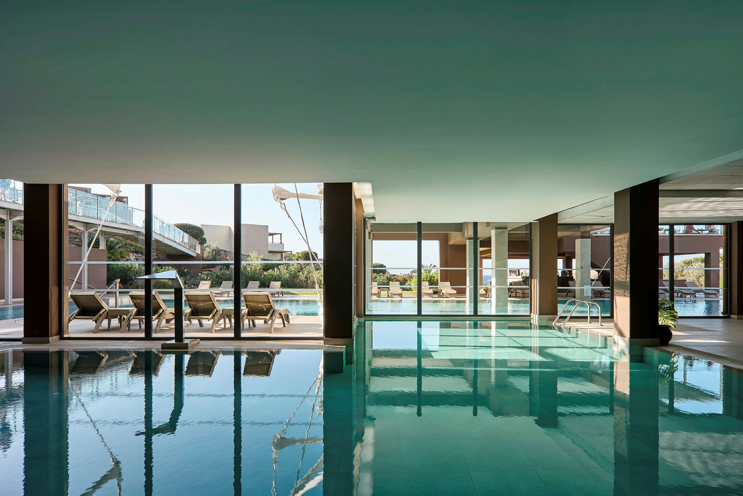 En indendørs pool med udsigt til en udendørs pool gennem store glasvinduer. (AI-genereret tekst)
