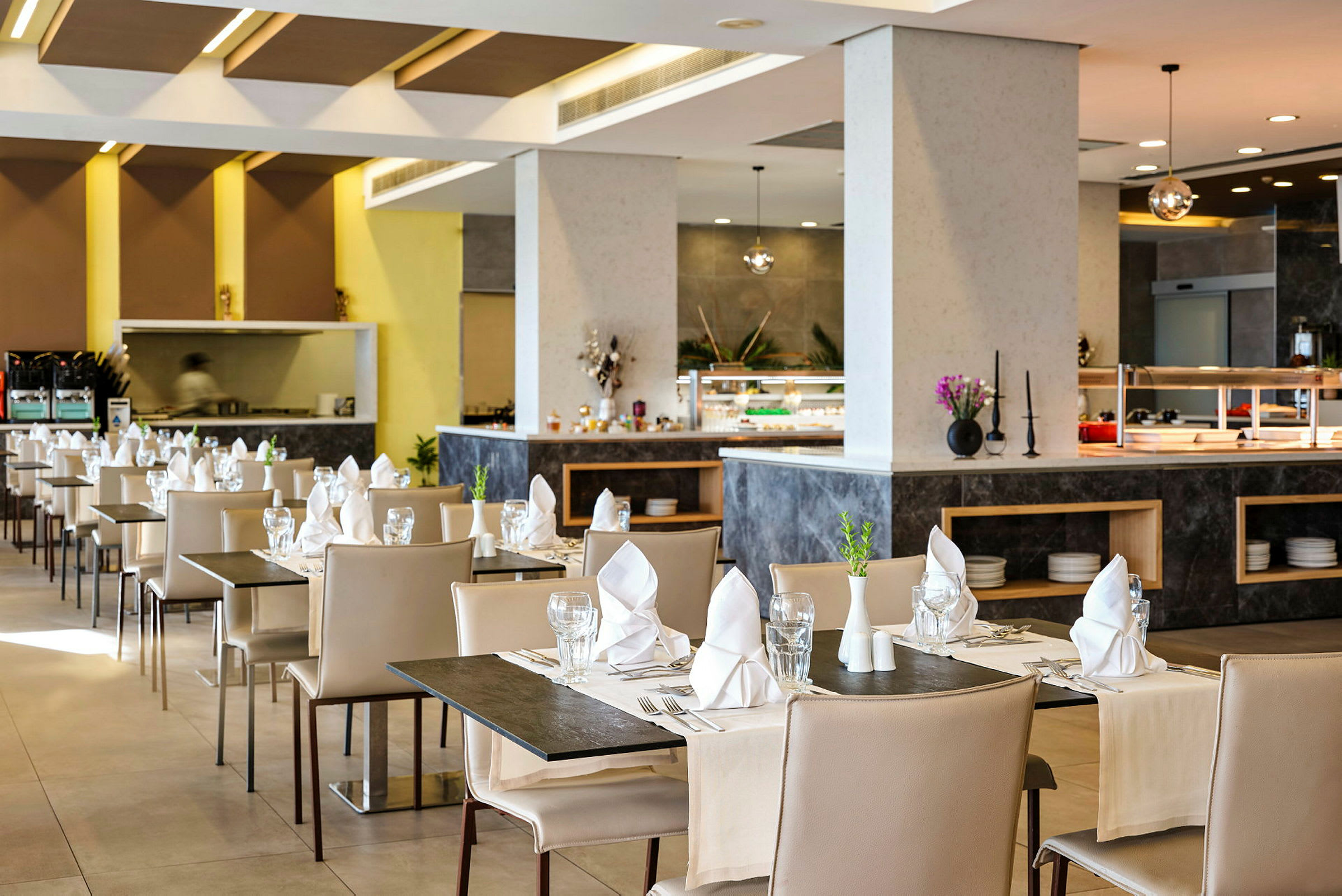 En moderne restaurant med dækkede borde, beige stole og servietter på hvert bord. (AI-genereret tekst)