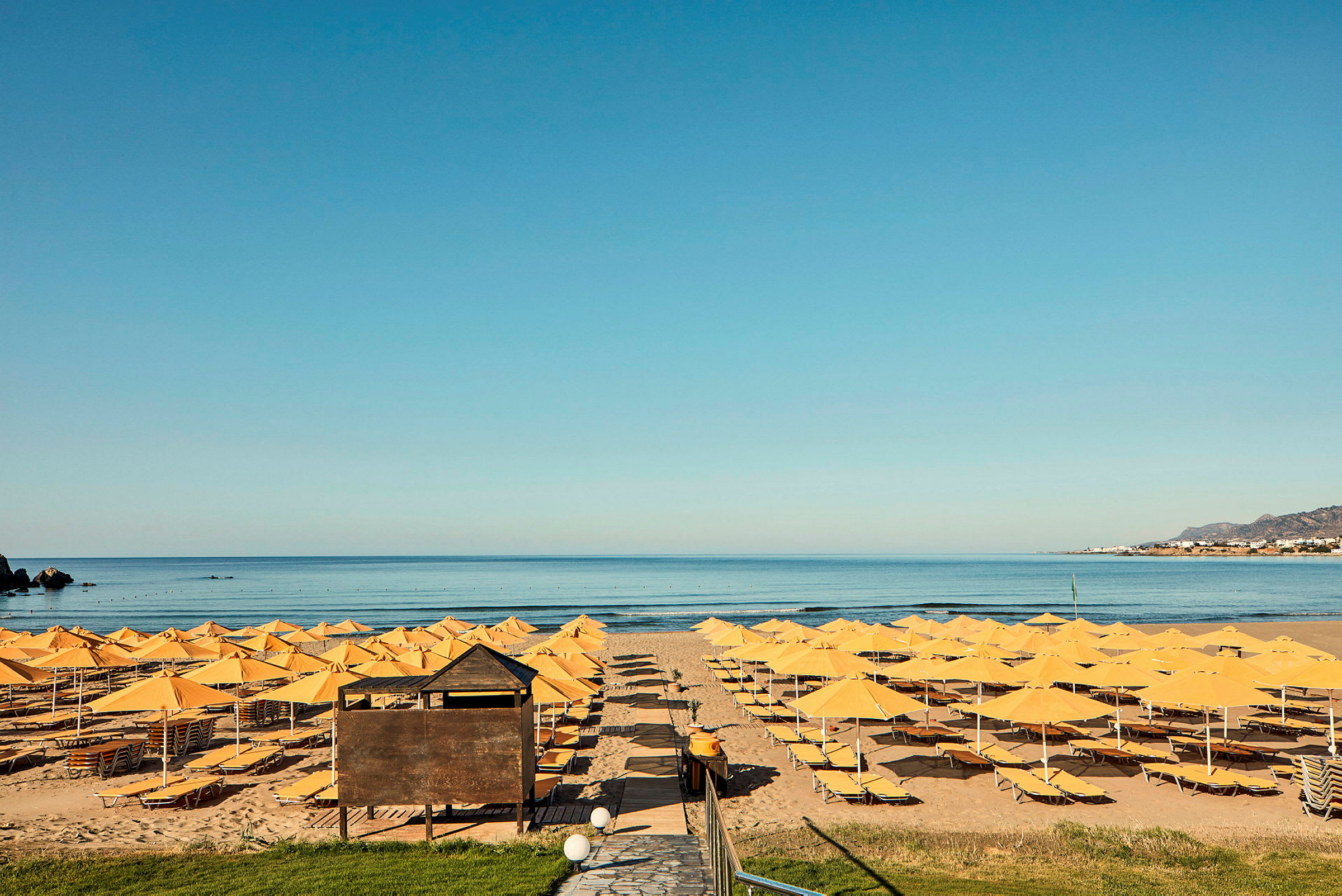 Strand med gule parasoller og liggestole foran havet. (AI-genereret tekst)