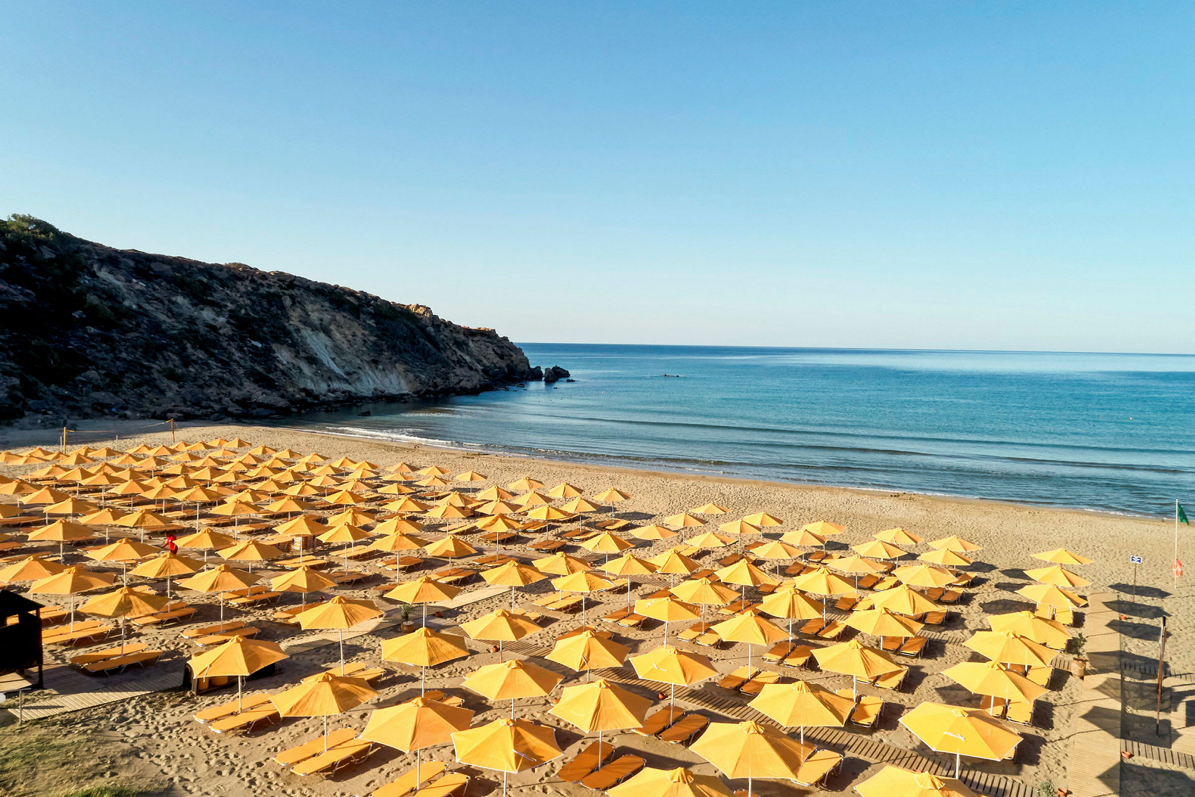 Gule parasoller er placeret på en solrig strand nær en klippe. (AI-genereret tekst)