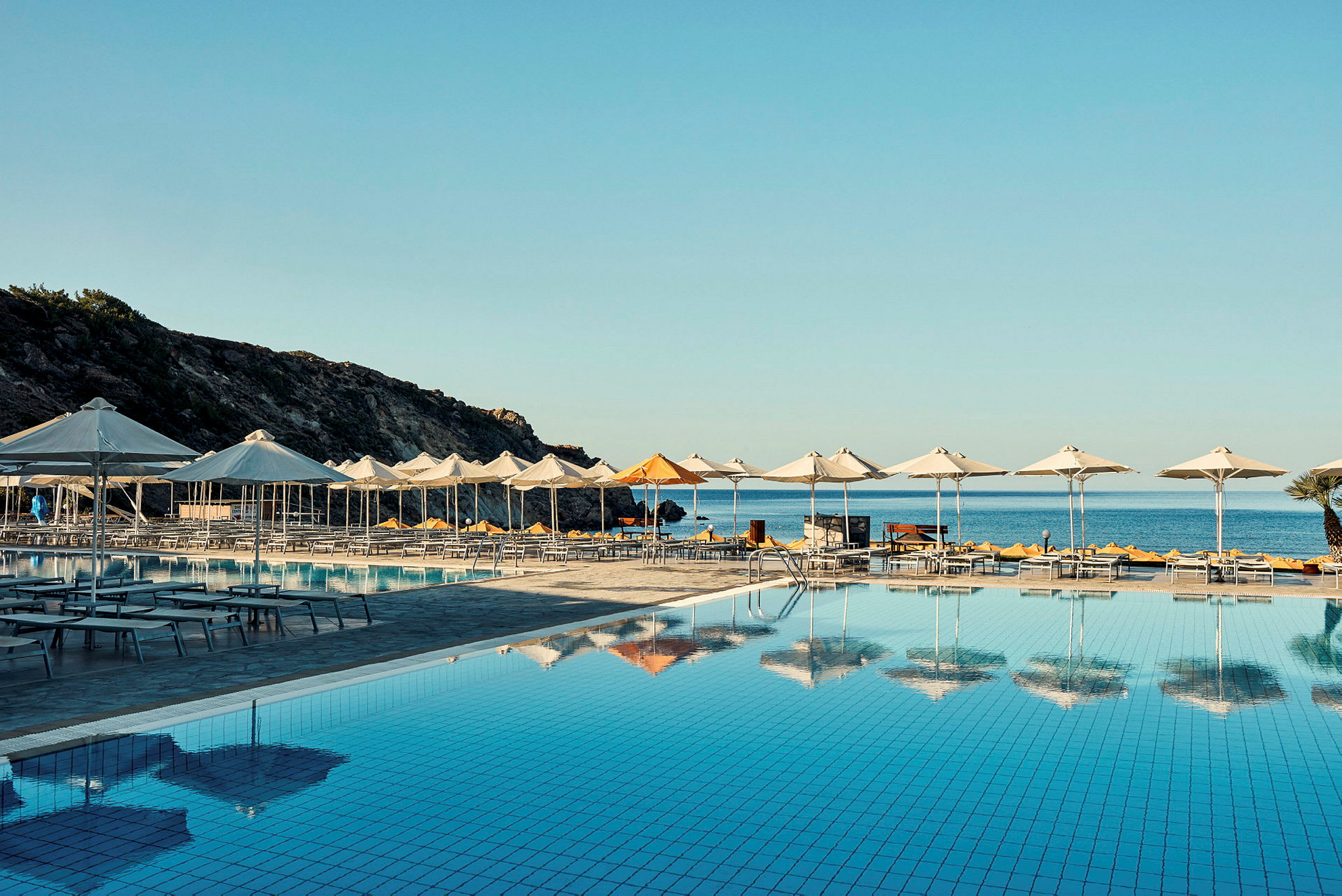 Swimmingpool område med parasoller foran havet. (AI-genereret tekst)