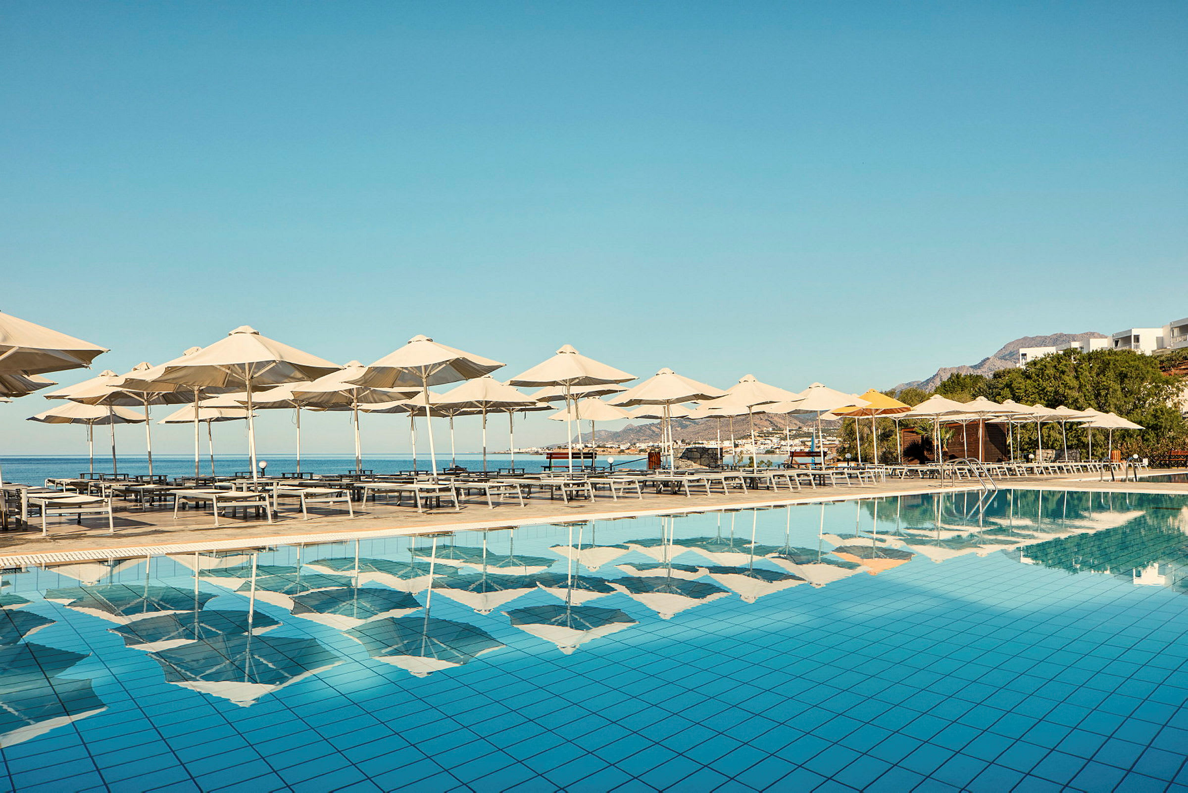 Solsenge og parasoller ved en pool med udsigt over havet. (AI-genereret tekst)