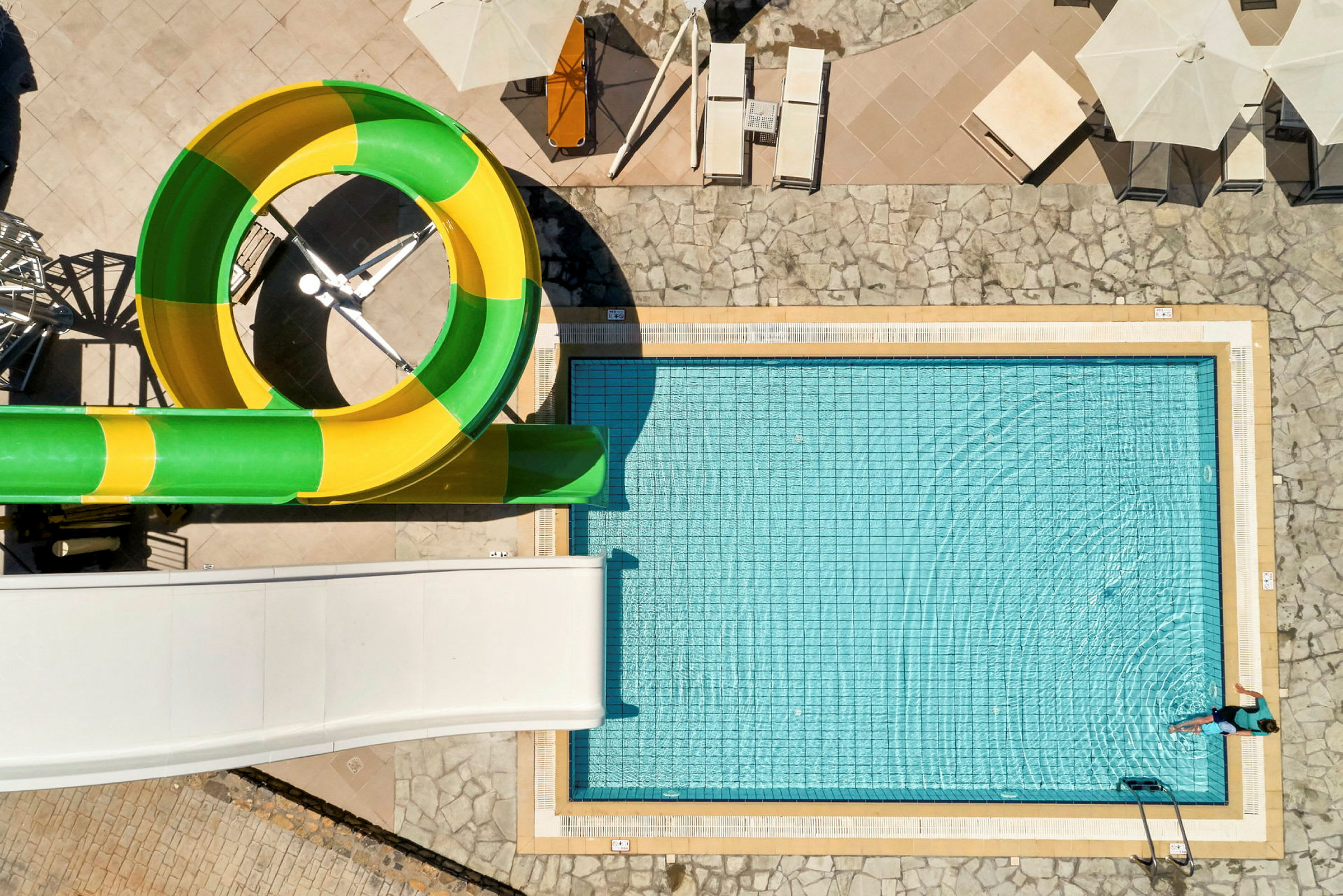 Udendørs swimmingpool med gul og grøn vandrutsjebane. (AI-genereret tekst)