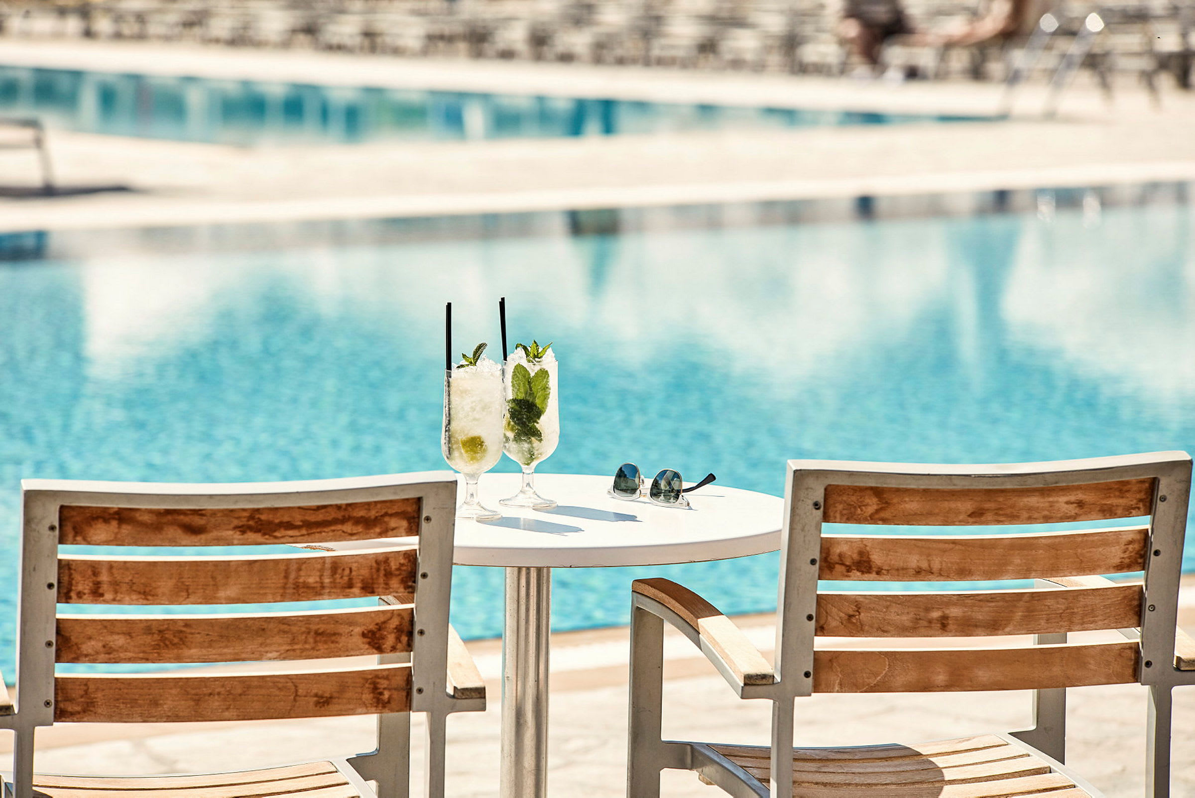 To liggestole og et bord med to glas med drinks ved en pool. (AI-genereret tekst)