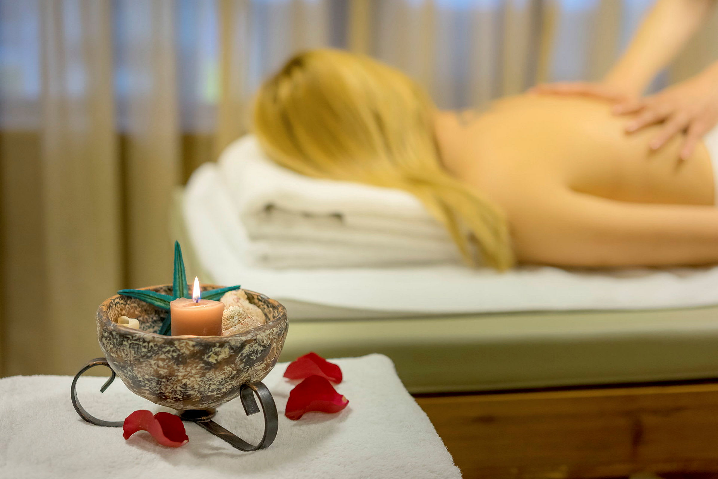 En massagebriks med en person liggende under behandling. En dekoration med et tændt lys og blomster i forgrunden. (AI-genereret tekst)