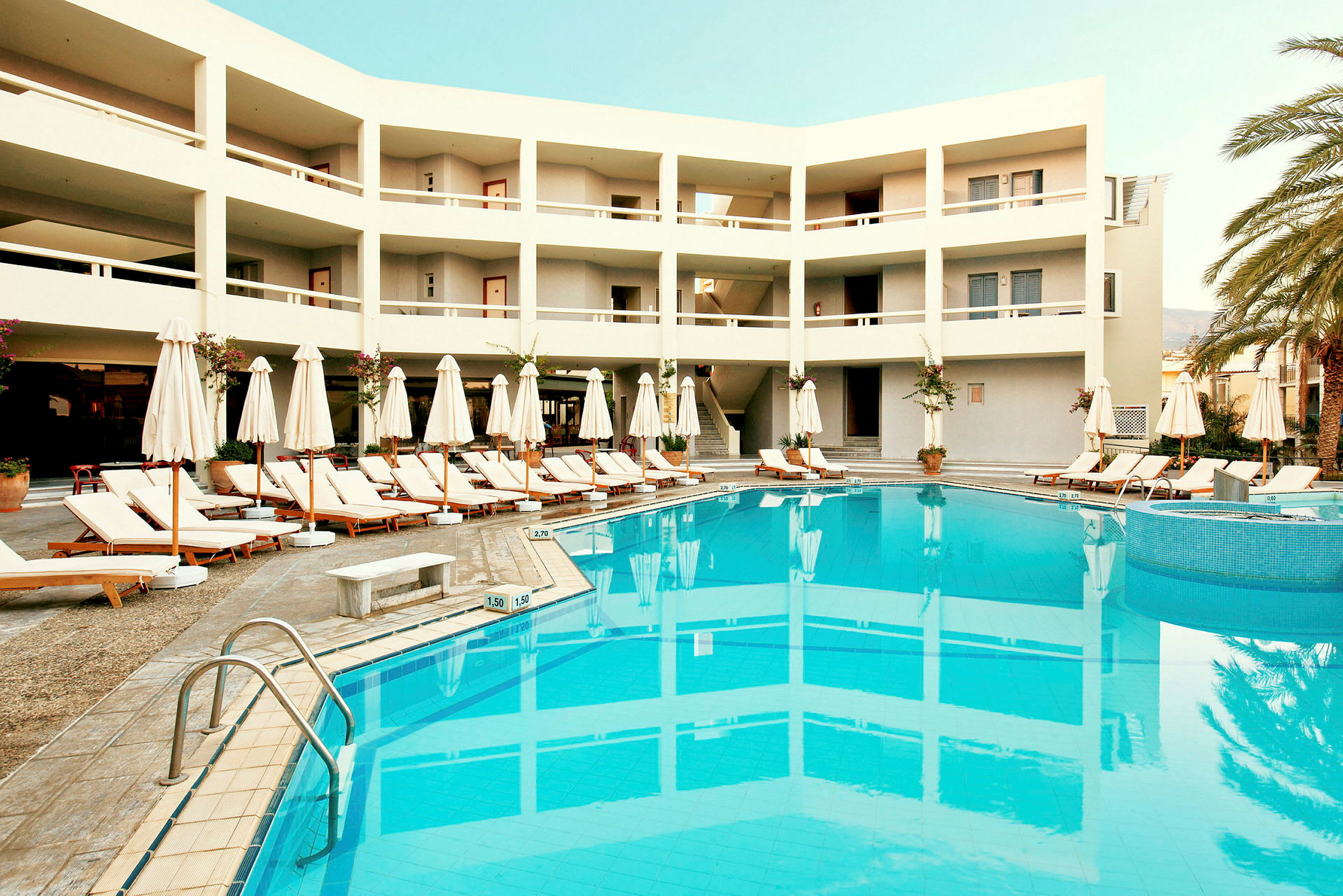 Hotelbygning med en pool og liggestole. (AI-genereret tekst)