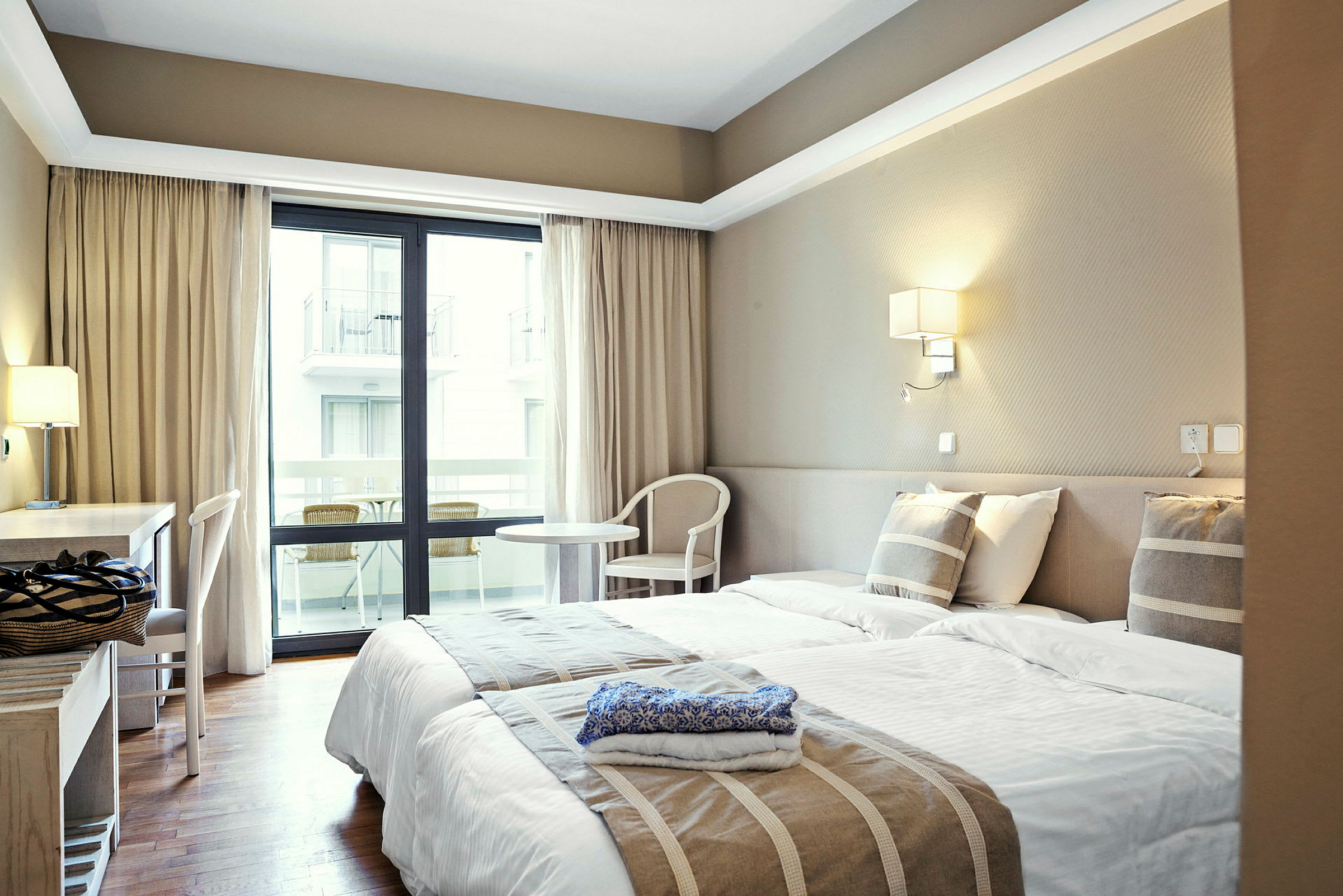 Hotelværelse med to enkeltsenge, skrivebord og altan. (AI-genereret tekst)