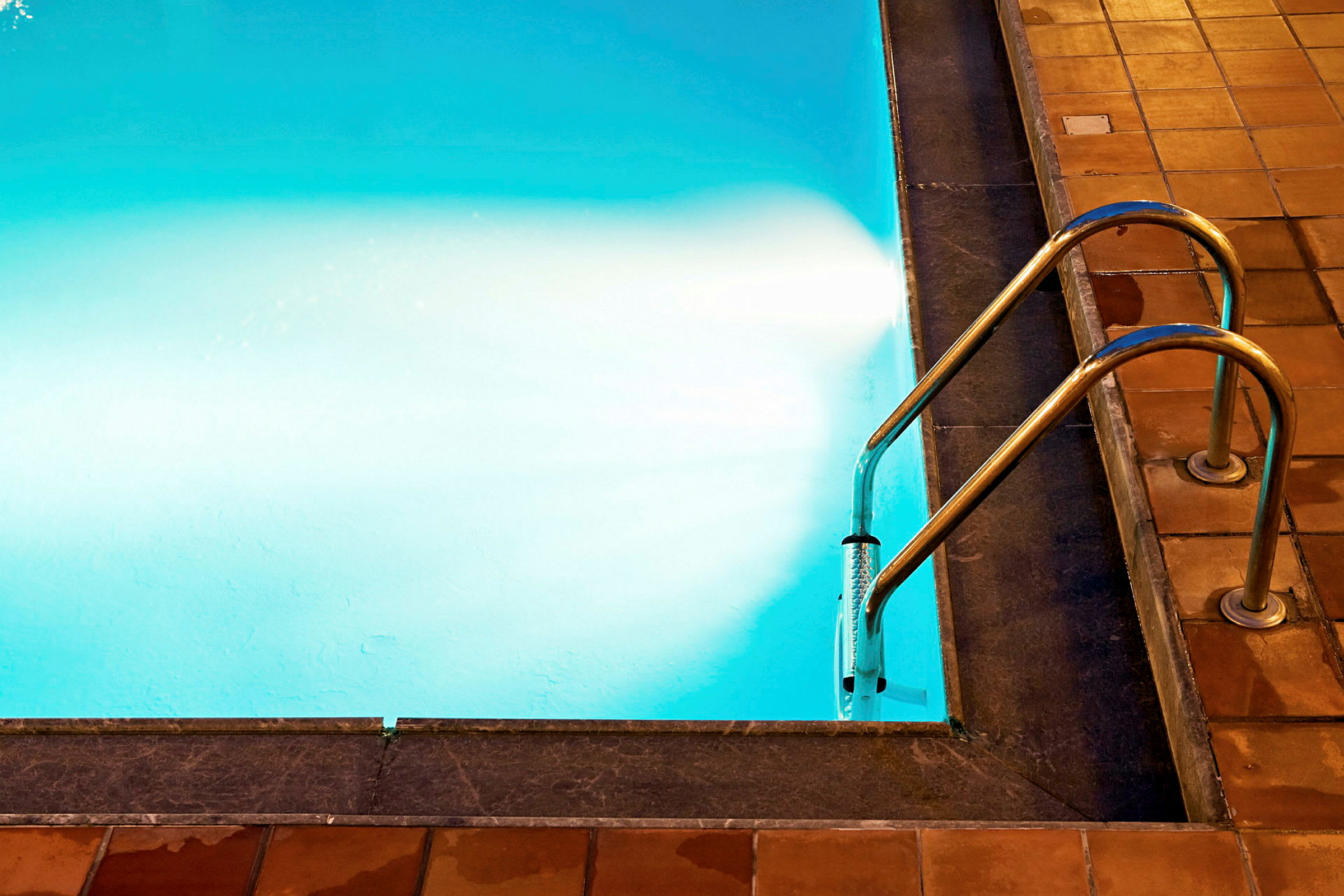 Billede af en swimmingpoolkant med gelænder og vand. (AI-genereret tekst)