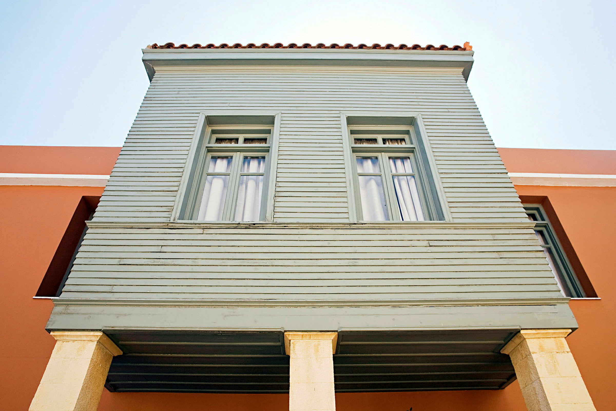 To store vinduer på en lysegrøn træfacade støttet af søjler. (AI-genereret tekst)