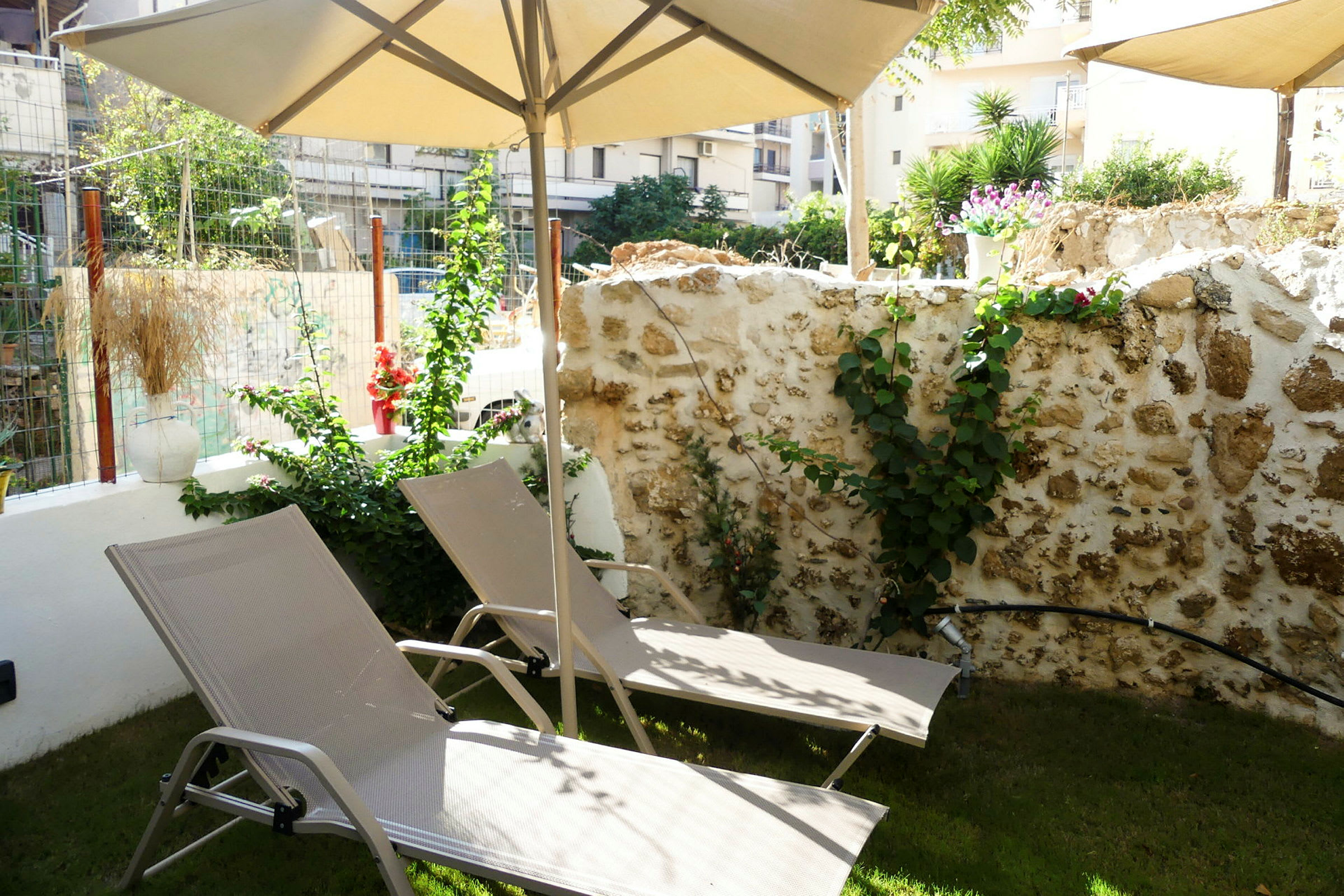 To liggestole under en parasol foran en stenmur med planter. (AI-genereret tekst)