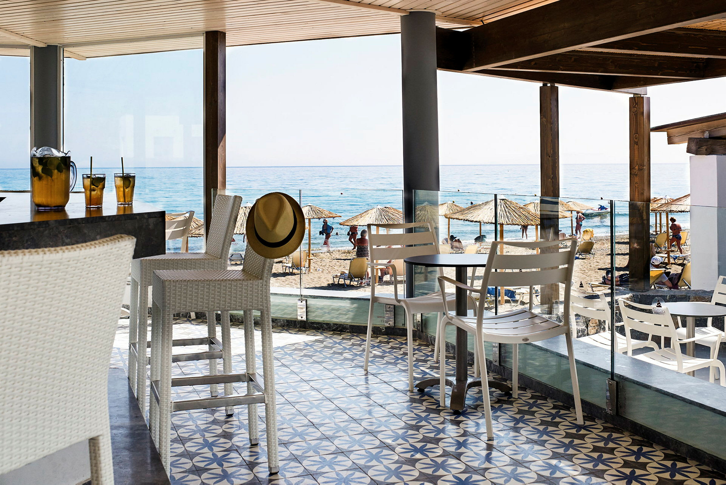 En strandbar med hvidt interiør. I baggrunden ses en sandstrand og havet. (AI-genereret tekst)