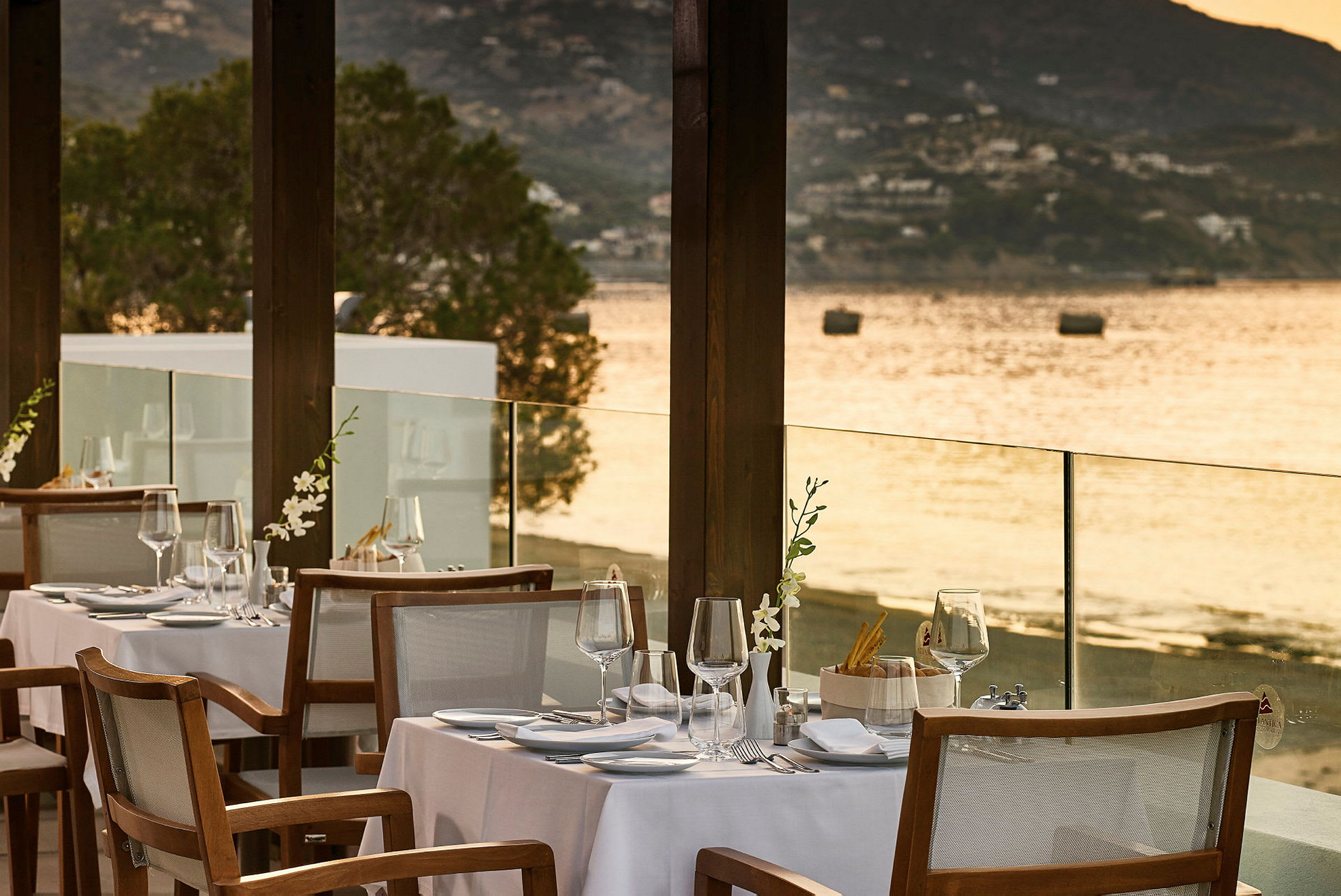En udendørs restaurant med dækkede borde ved vandet og udsigt over havet. (AI-genereret tekst)
