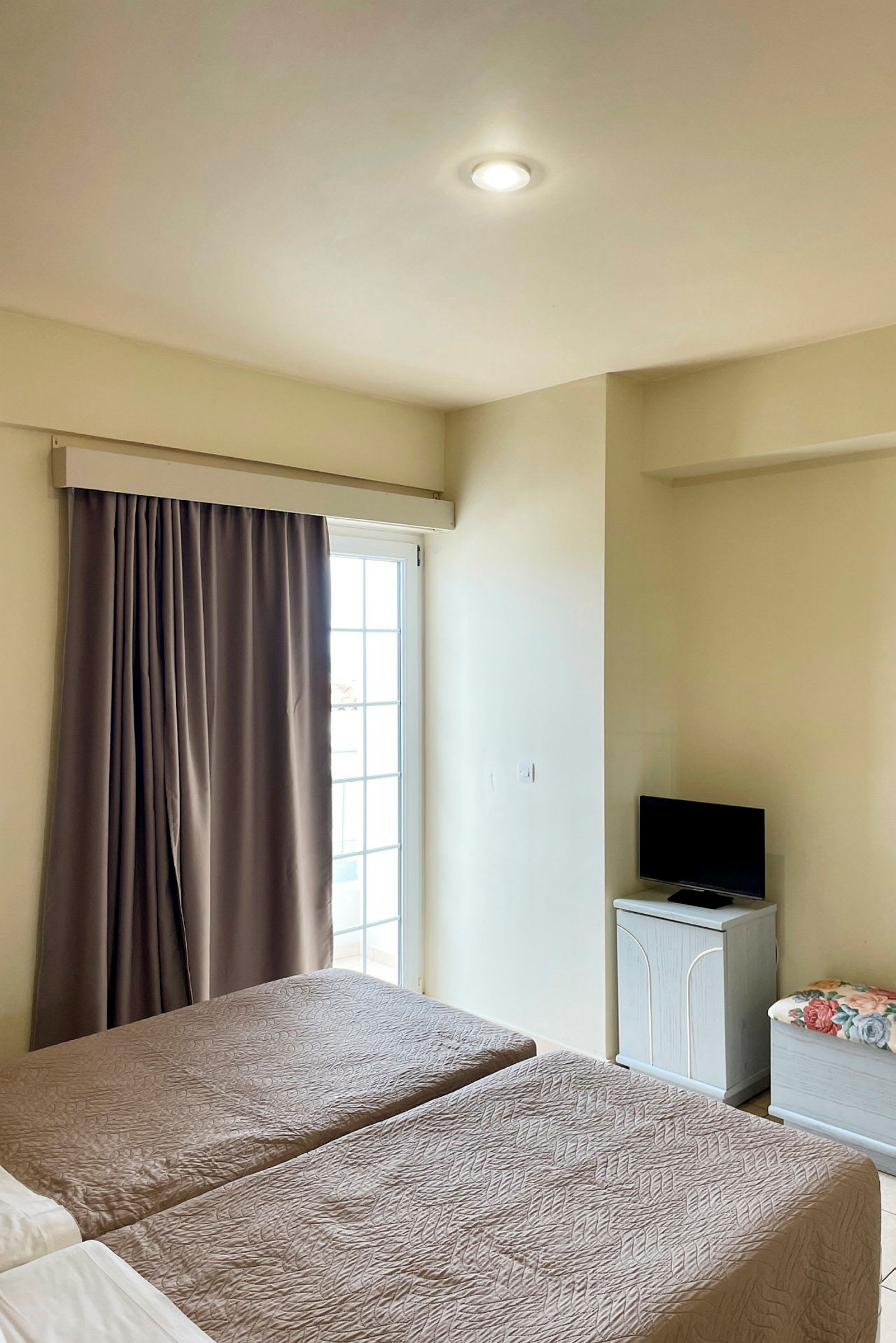 Et hotelværelse med to enkeltsenge, en altandør med gardin og et lille TV på et skab. (AI-genereret tekst)