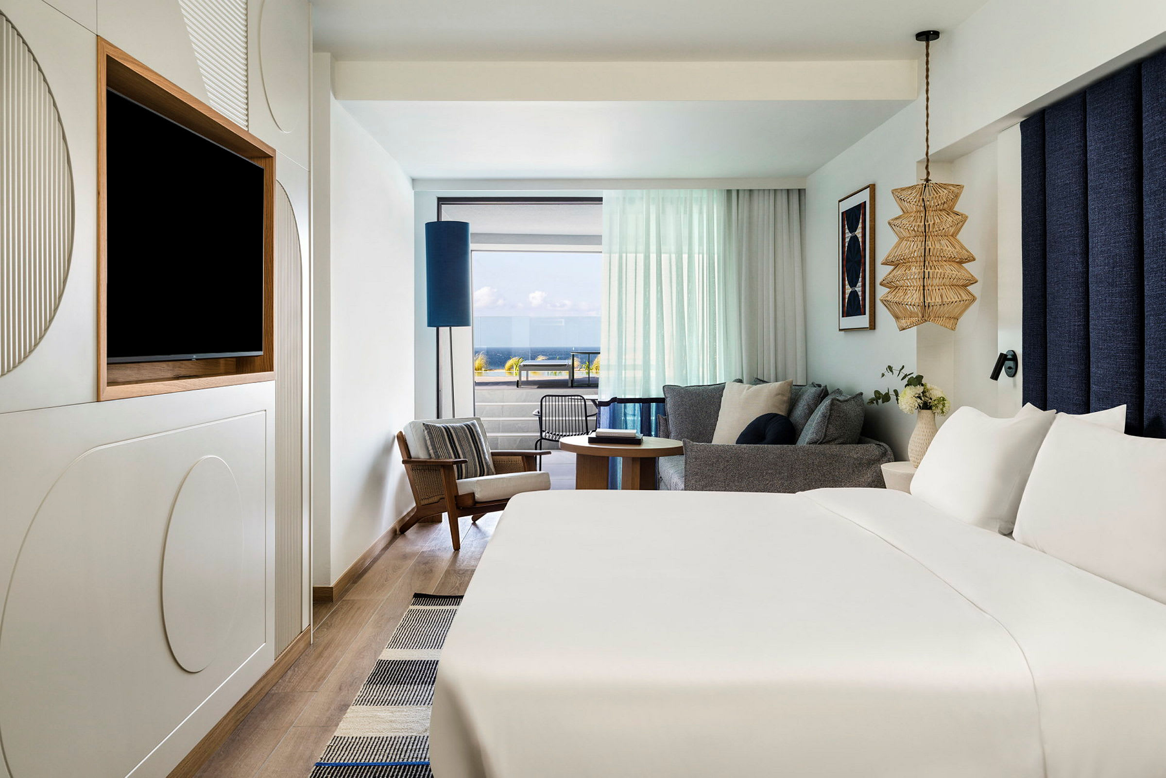 Et hotelværelse med stor seng, et siddeområde med glas mod altan og havudsigt. (AI-genereret tekst)
