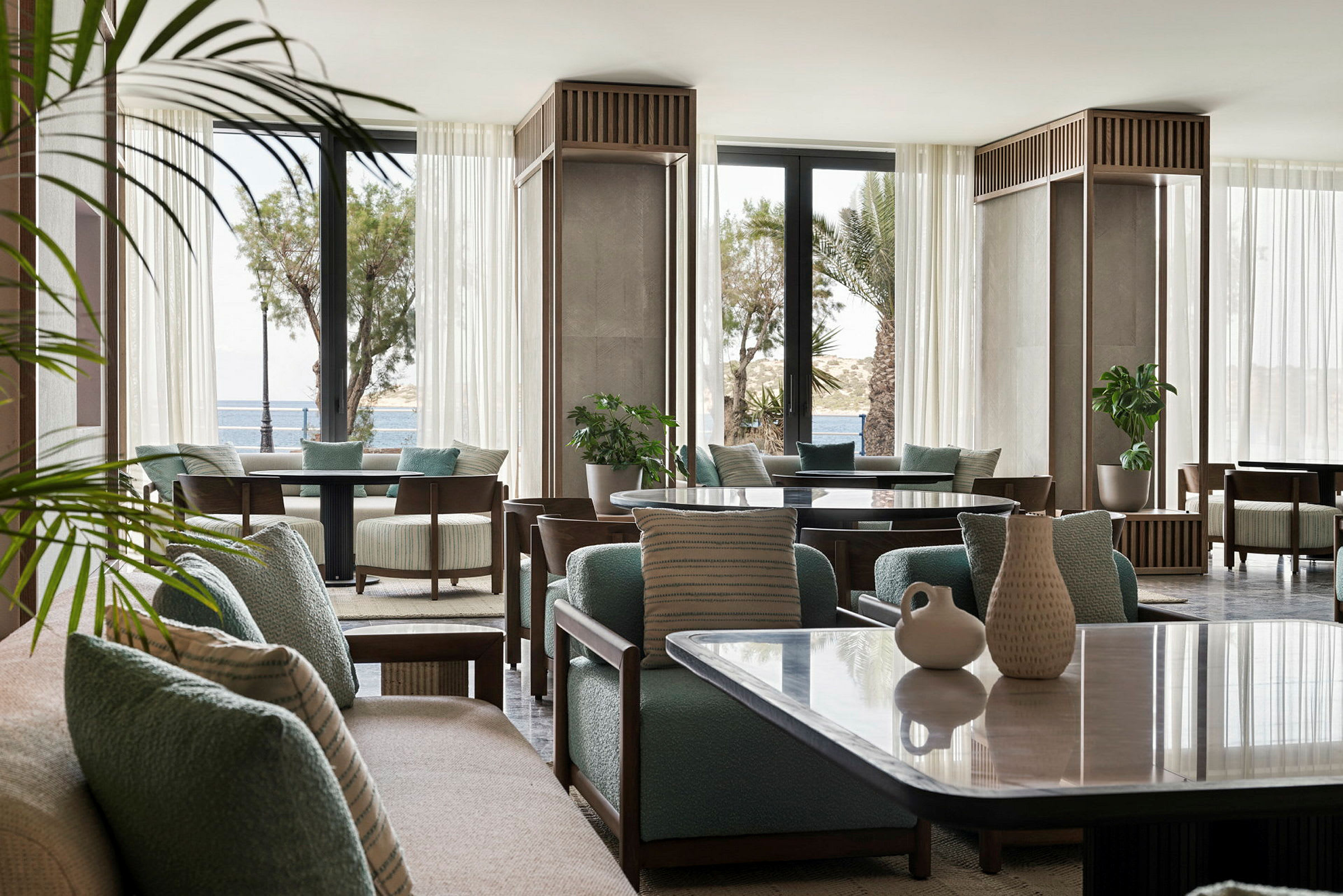 Interiør af et moderne rum med sofaer, borde og planter samt store vinduer med udsigt over havet. (AI-genereret tekst)