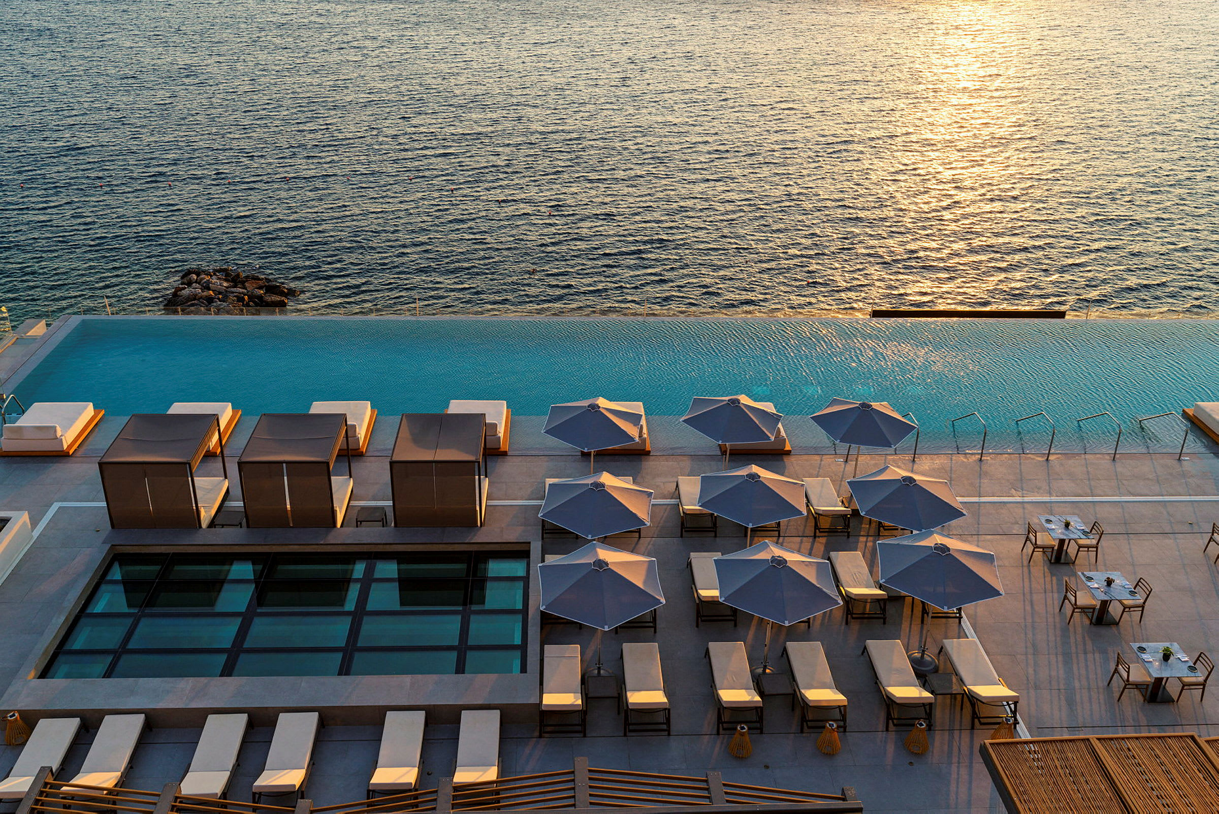 Billede af en pool med liggestole og parasoller ved havet. (AI-genereret tekst)