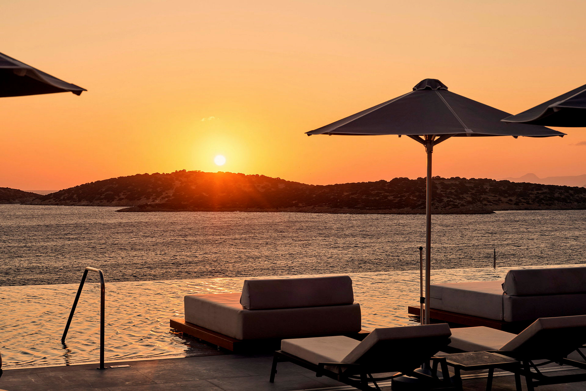 Solnedgang ved havet med solvogne og parasoller ved en infinity-pool. (AI-genereret tekst)