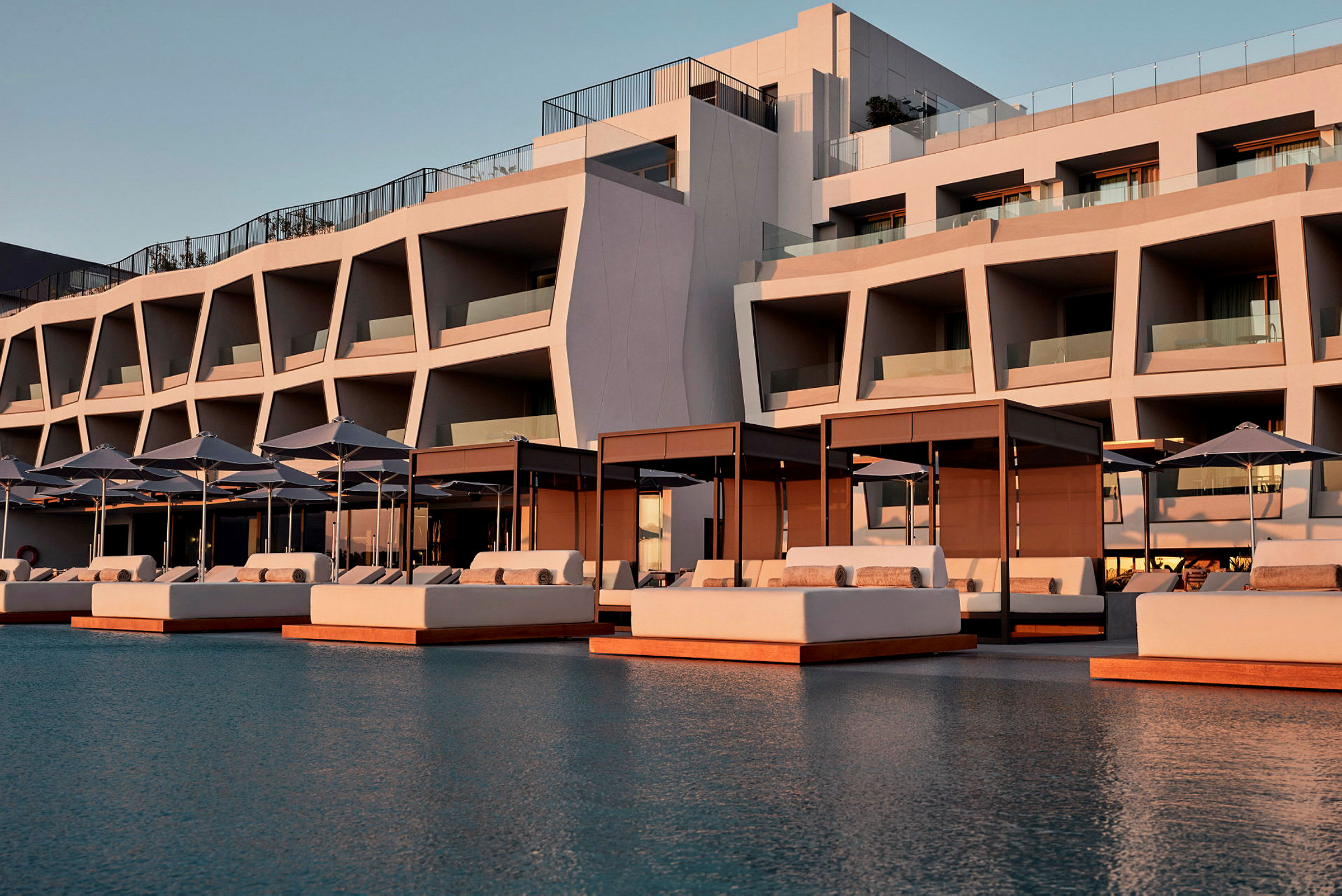 Moderne hotelbygning med solvogne og parasoller ved en pool. (AI-genereret tekst)