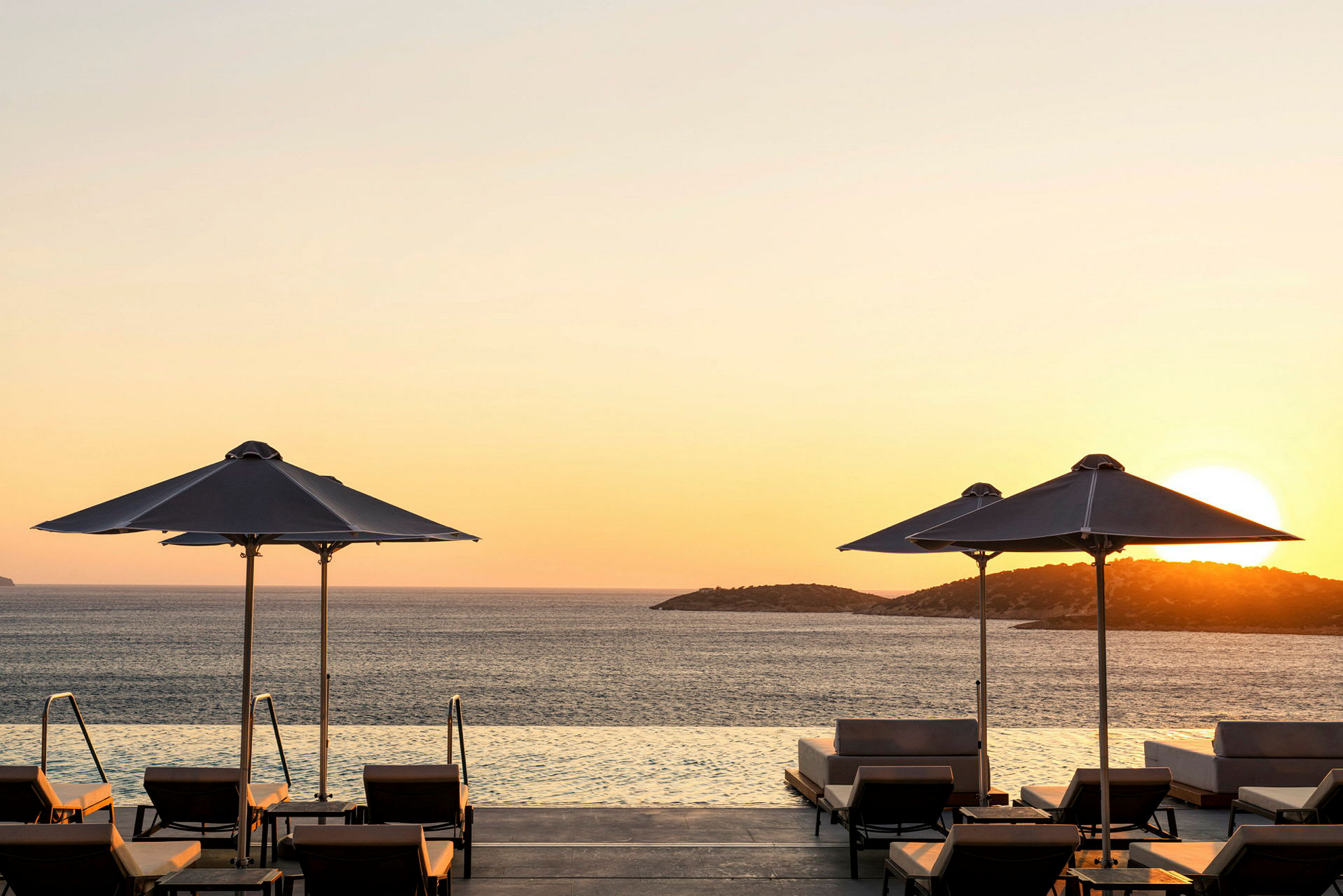 Udsigt over infinitypool med solnedgang og parasoller. (AI-genereret tekst)